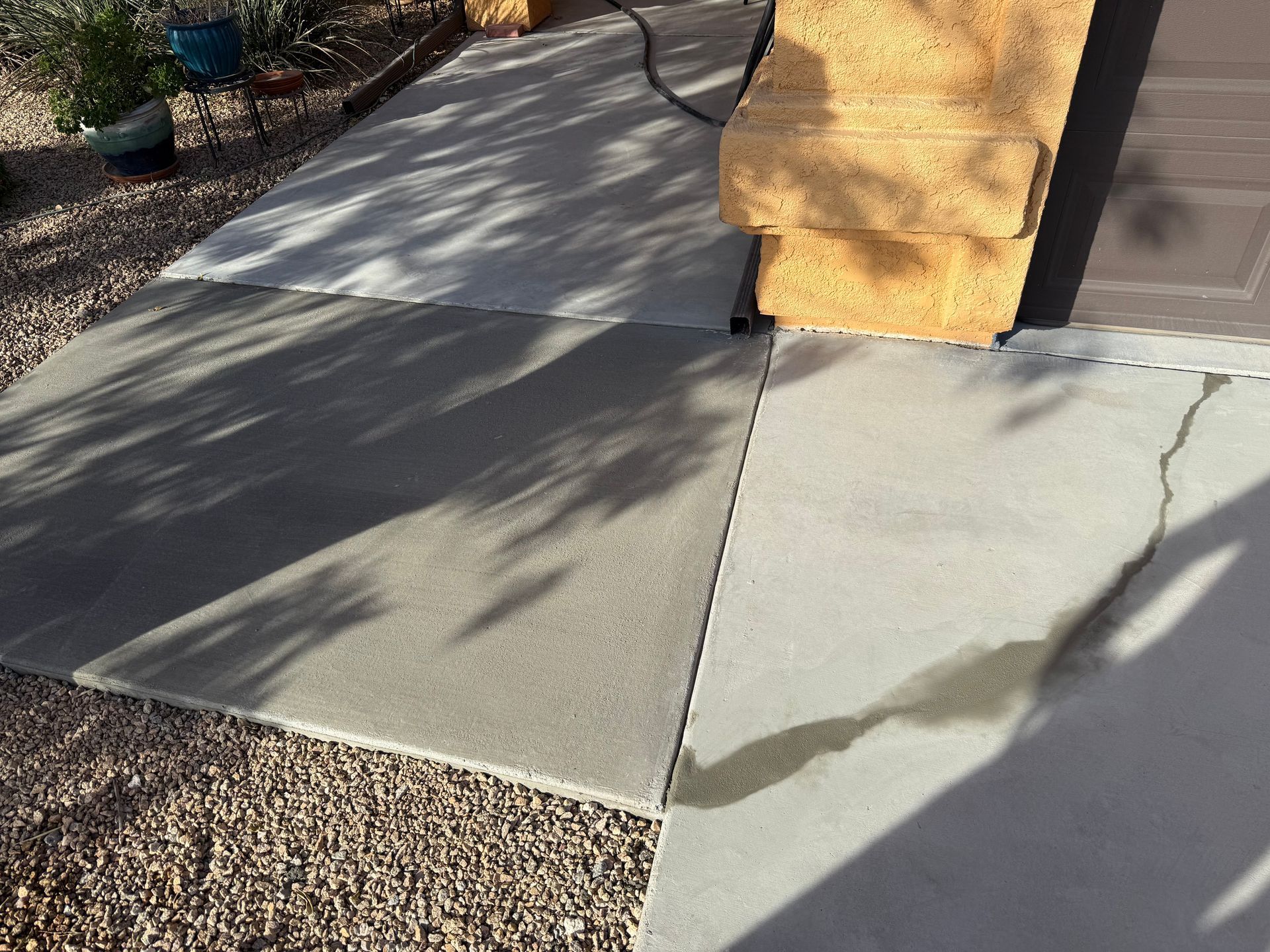 Sunlit sidewalk with cracked concrete beside a stucco wall and gravel path