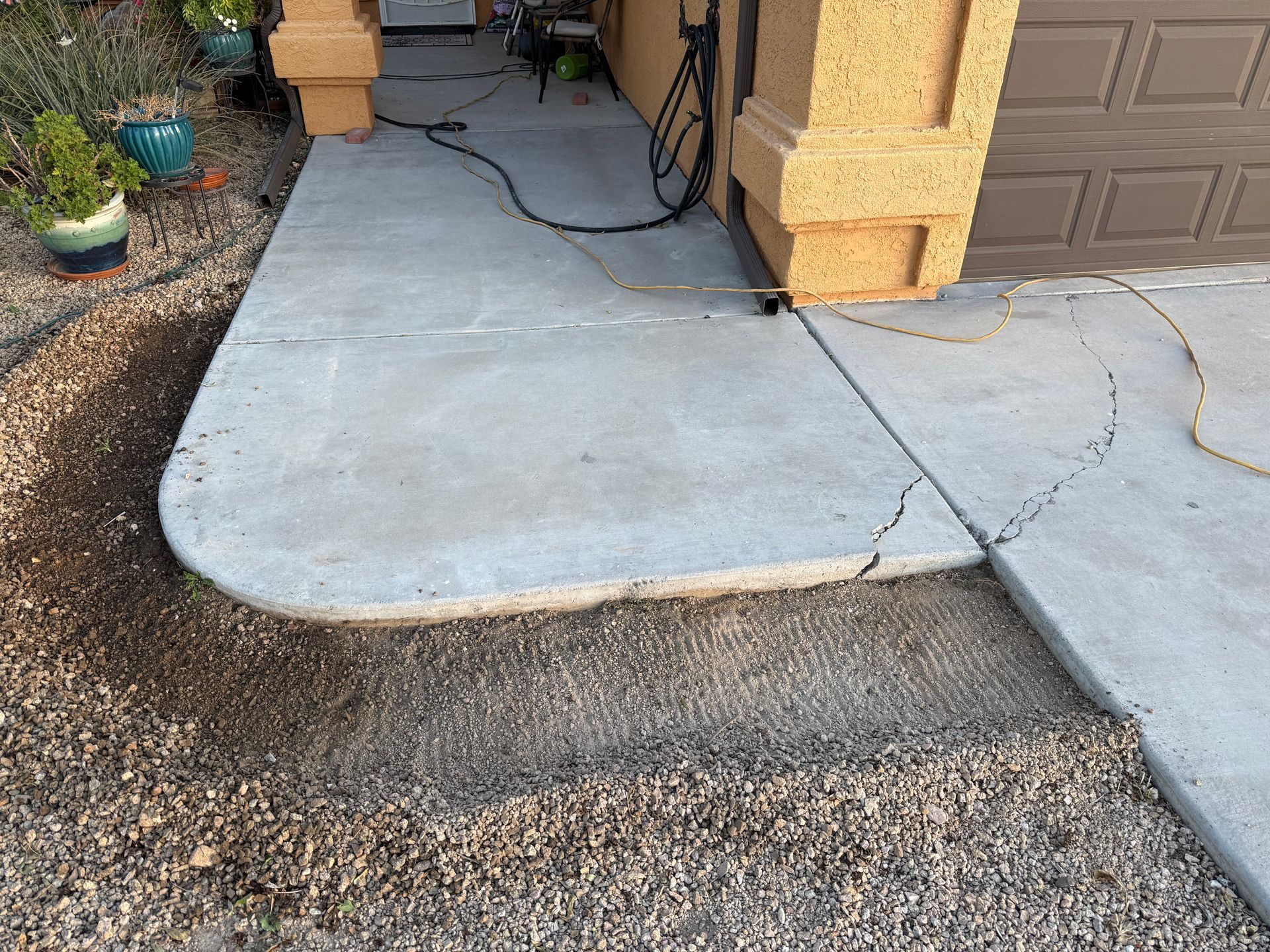Concrete sidewalk with a raised edge and a visible crack beside a stucco house entrance.