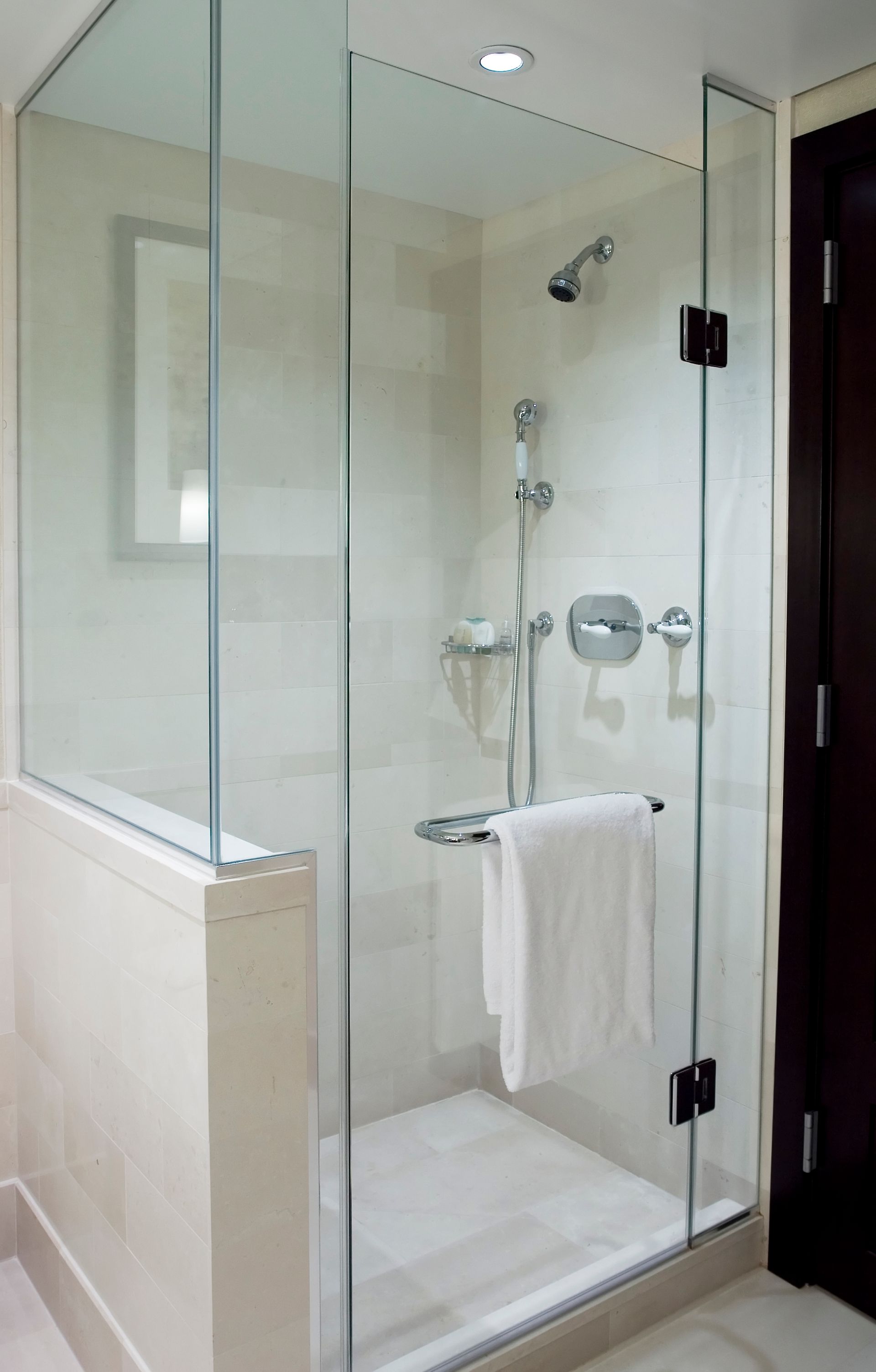 Glass walk-in shower with chrome fixtures and a towel hanging on the door