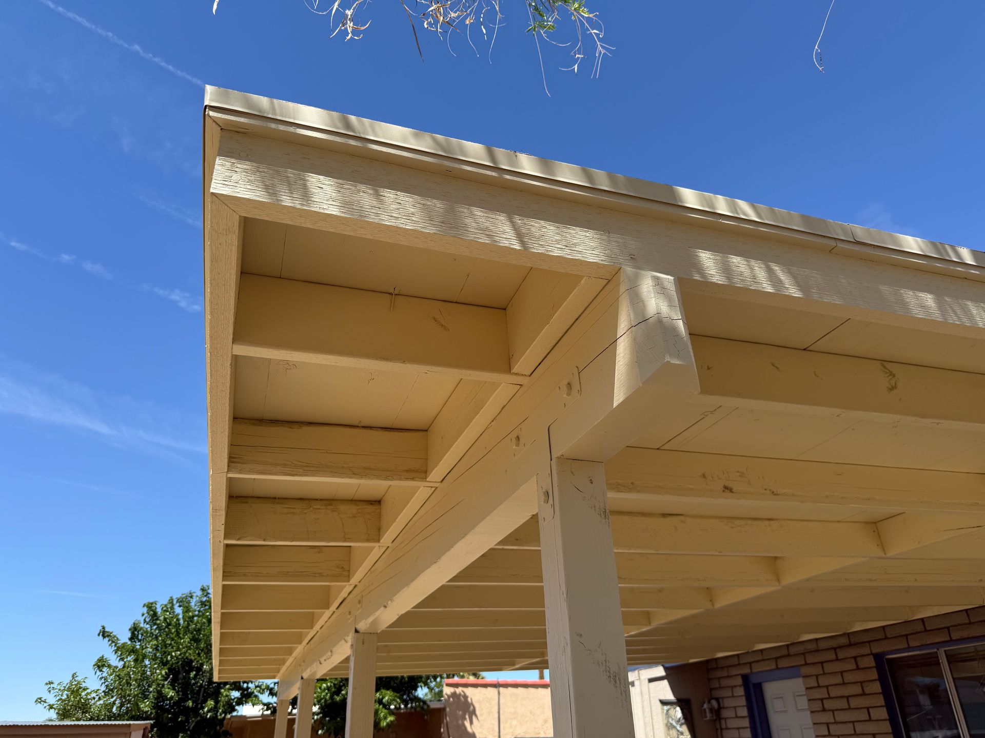 Yellow house eaves and support beams against a clear blue sky