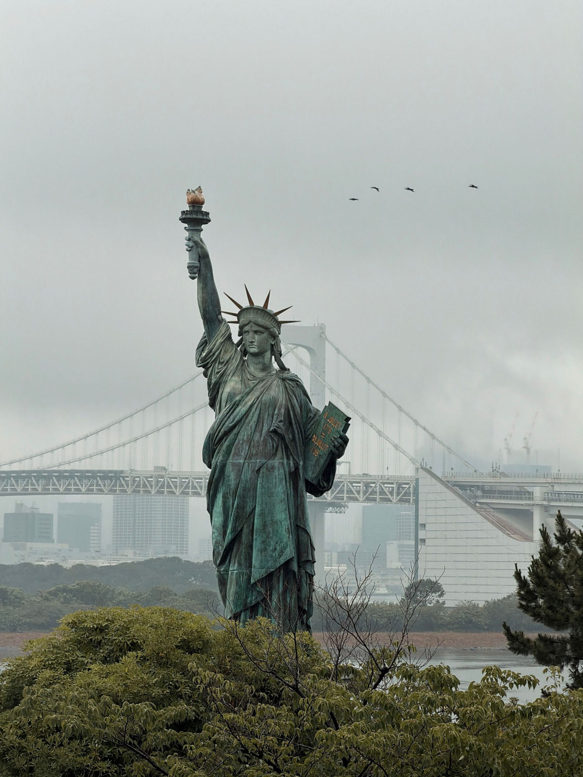 Statue of Liberty in fog with a bridge in the background over water