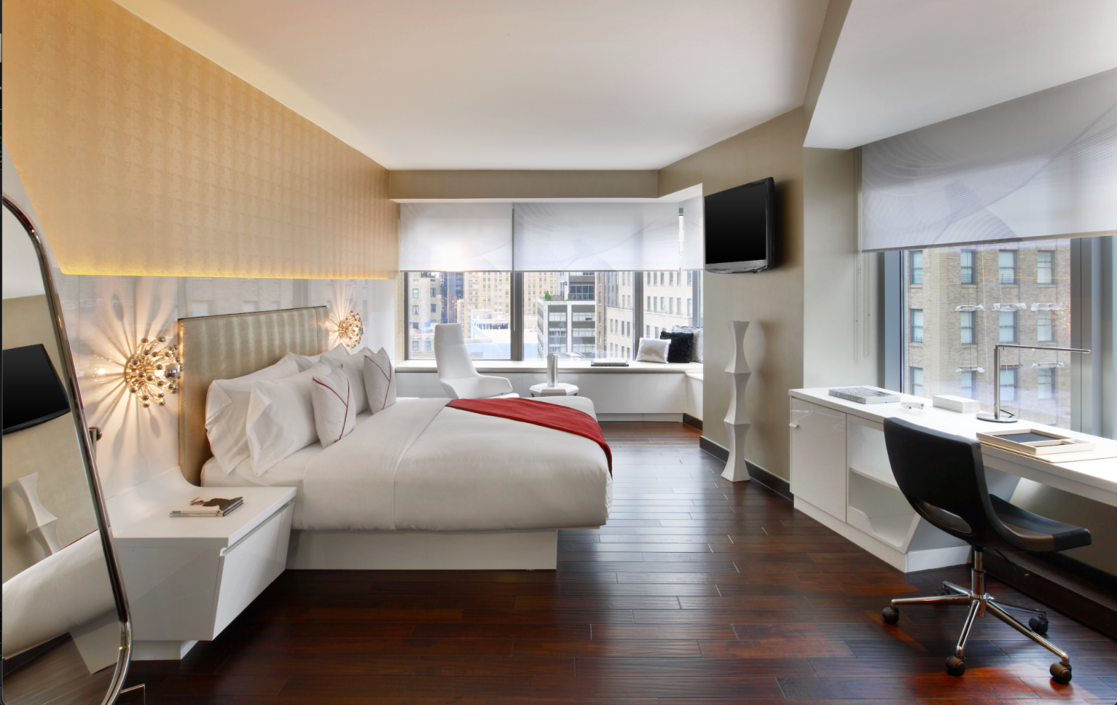 Modern hotel bedroom with large windows, white bed, desk, and dark wood floors