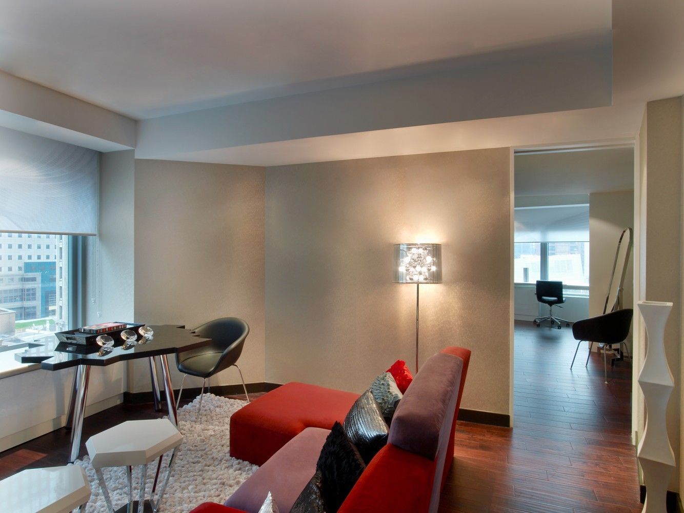 Modern apartment living room with red sofa, dining table, floor lamp, and city view through window