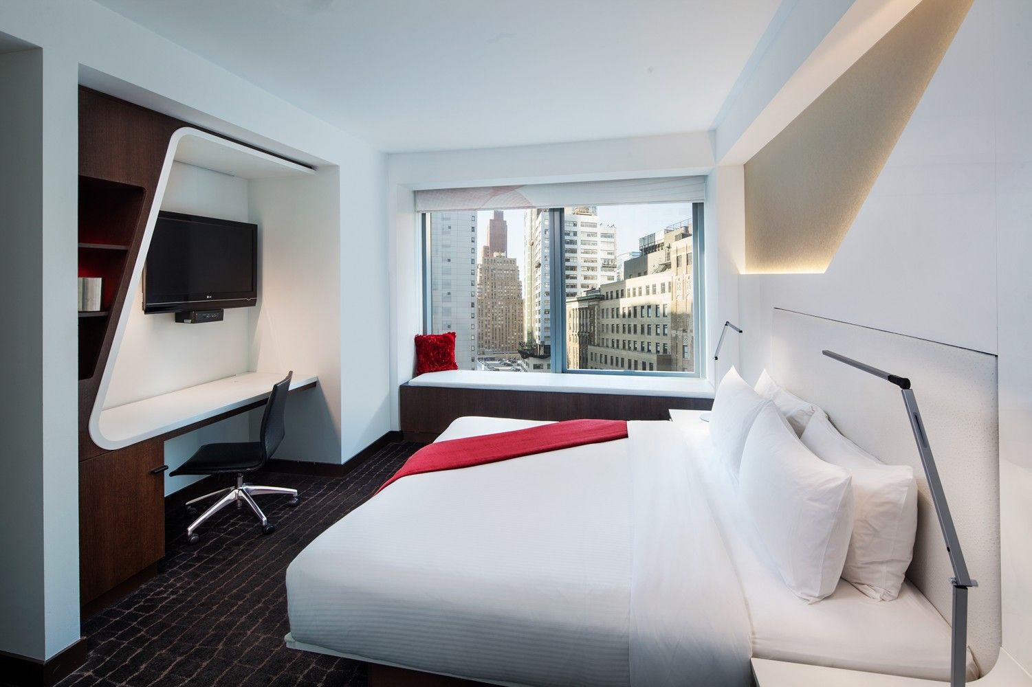 Modern hotel room with large bed, city view, desk, and wall-mounted TV