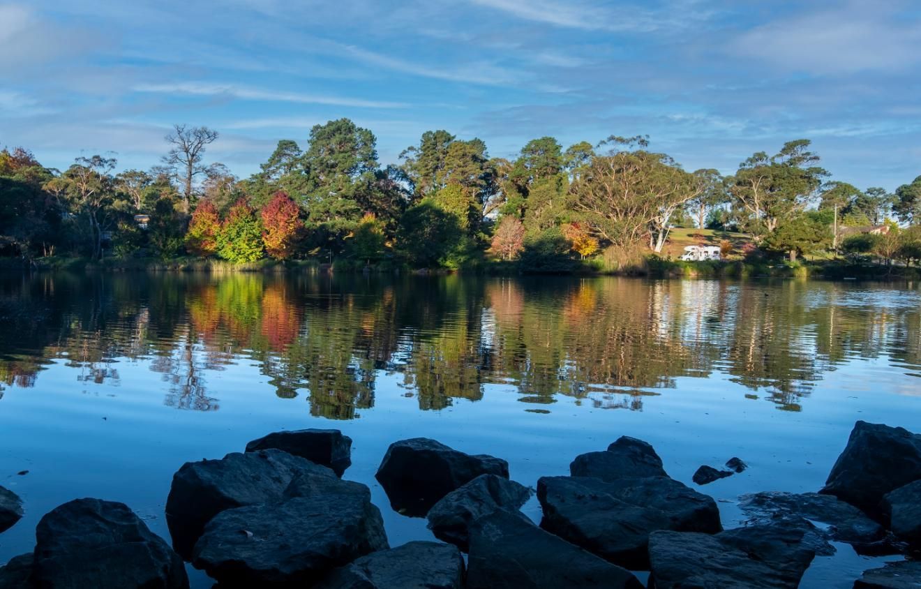 Still Water Reflects Trees with Fall Foliage Under a Blue Sky, Rocks in Foreground — JSF Interiors Goulburn in Mittagong, NSW