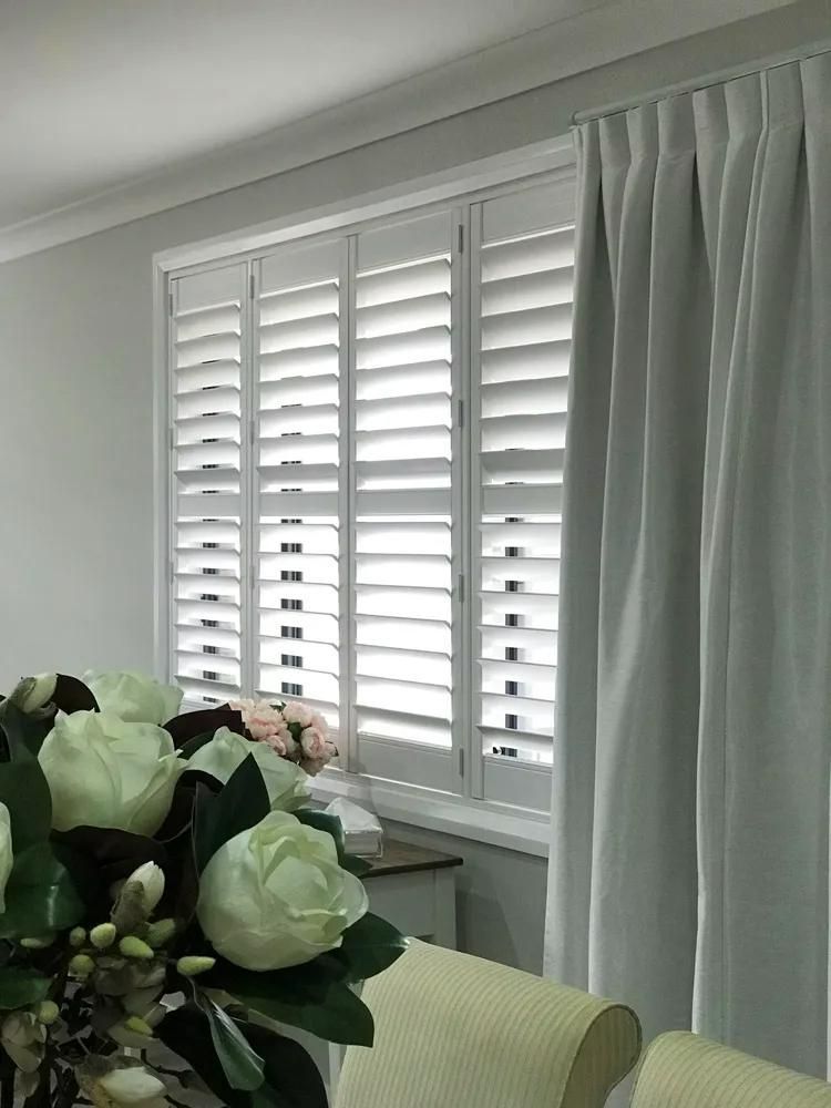 White shutters and light gray curtains frame a window, with a bouquet of white flowers in the foreground — JSF Interiors Goulburn in Goulburn, NSW