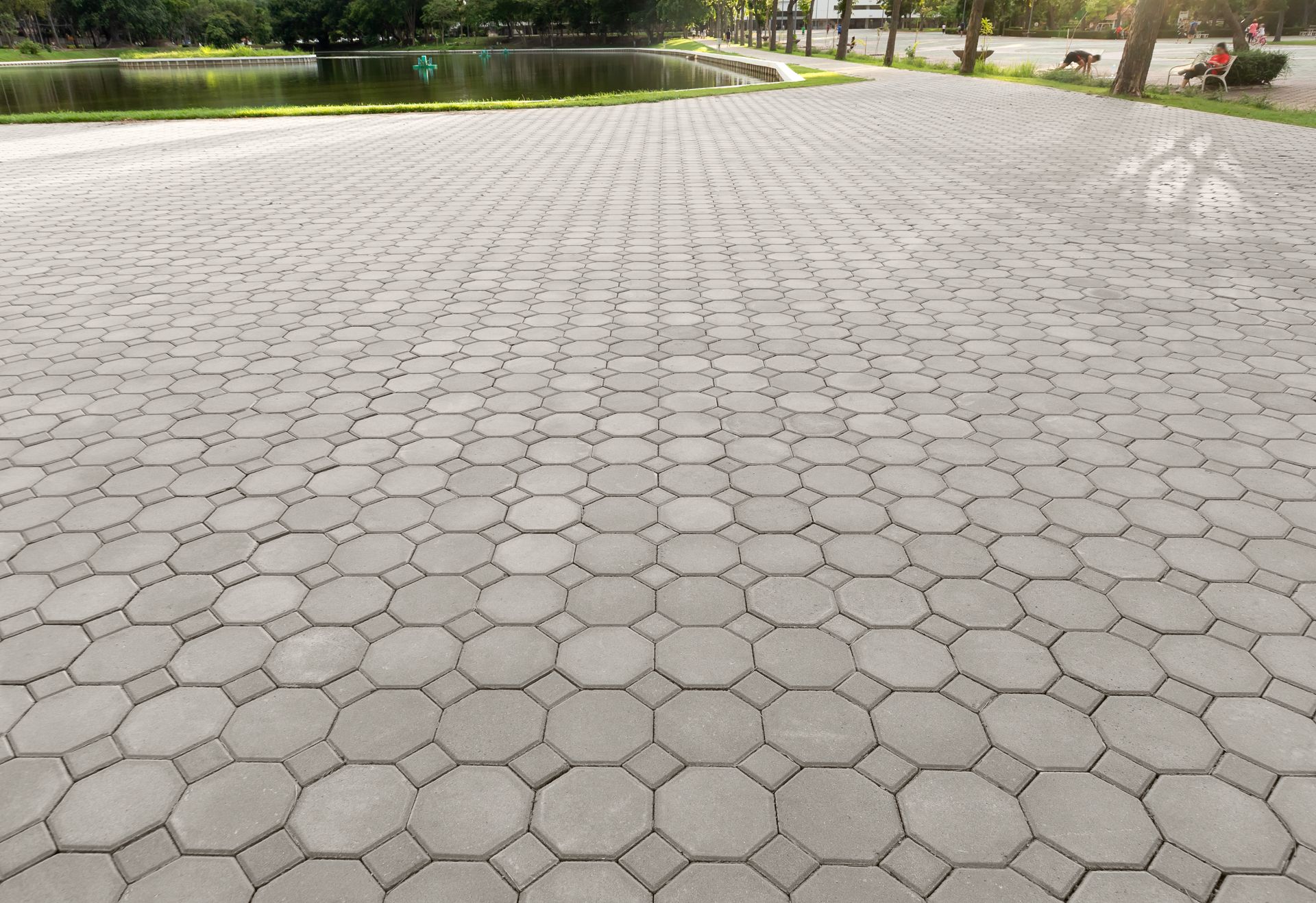 A brick walkway in a park with a lake in the background