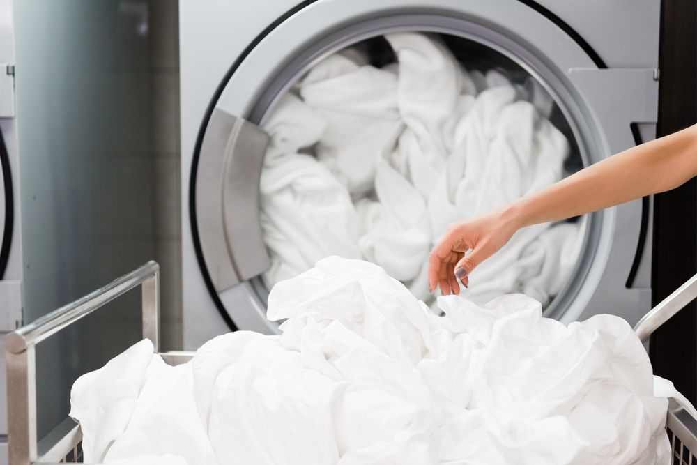 Persona che carica lenzuola bianche in una lavatrice commerciale in una lavanderia a gettoni.