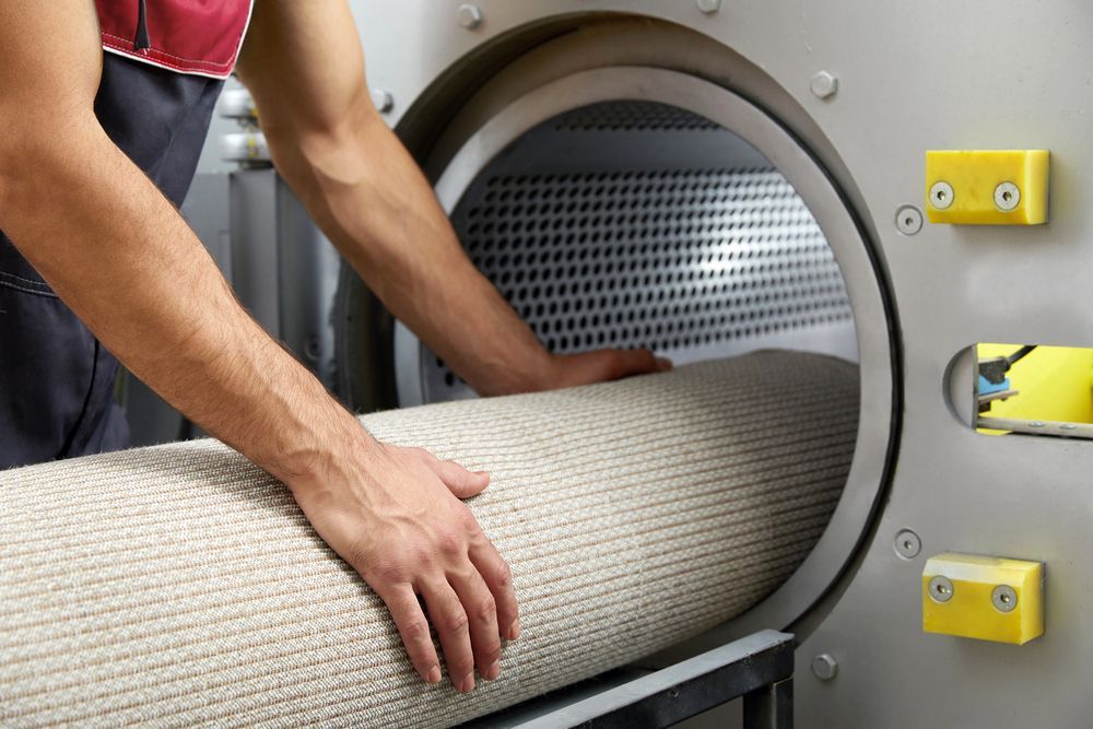 Uomo che carica un tappeto arrotolato in una grande macchina per la pulizia, probabilmente per una pulizia commerciale.