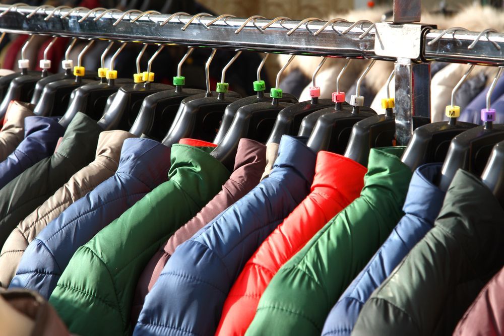 Cappotti di vari colori sono appesi su un attaccapanni, probabilmente in un negozio o in un mercato all'aperto.
