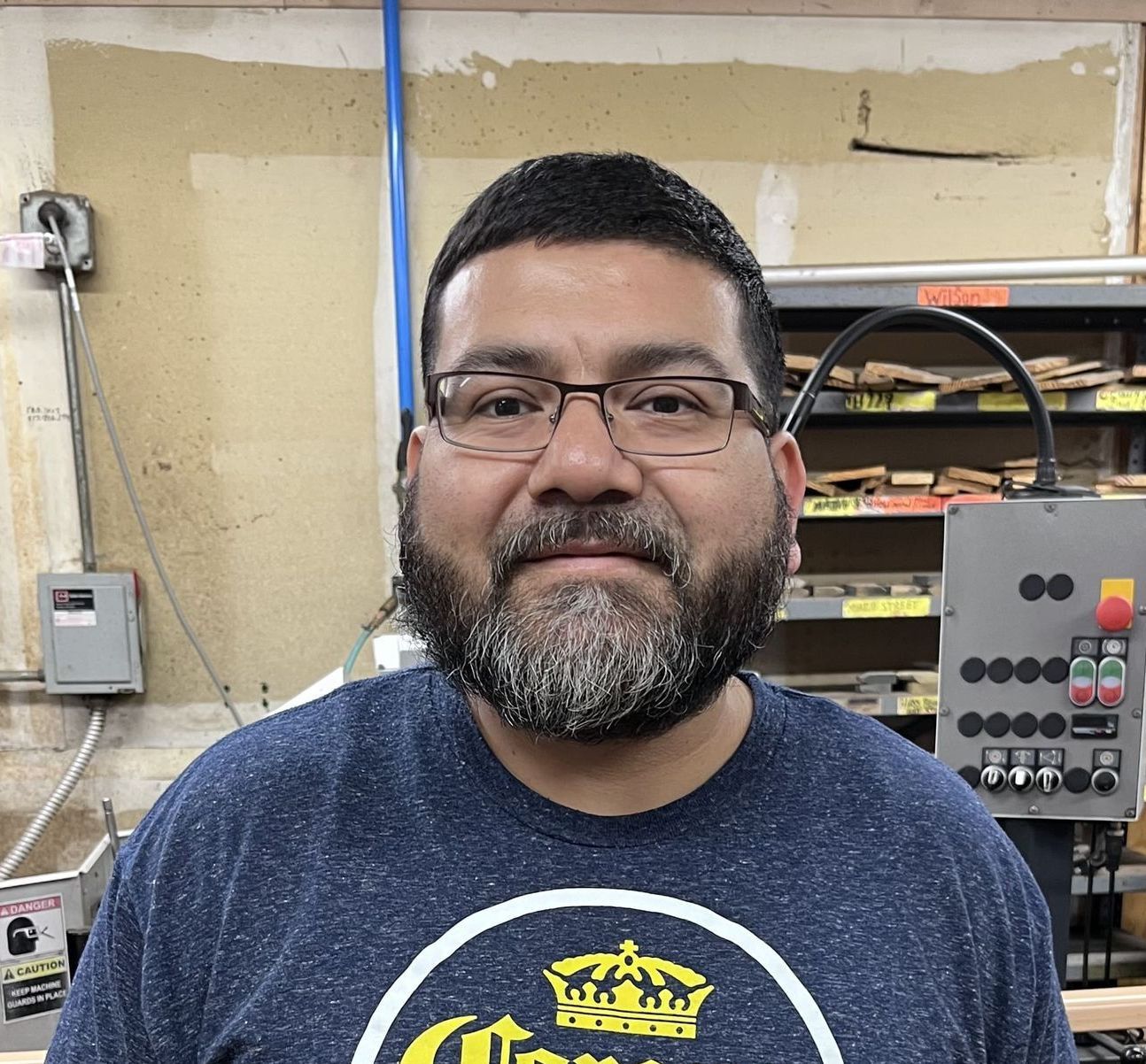 A man with a beard and glasses wearing a blue t-shirt, posing in what appears to be a workshop.