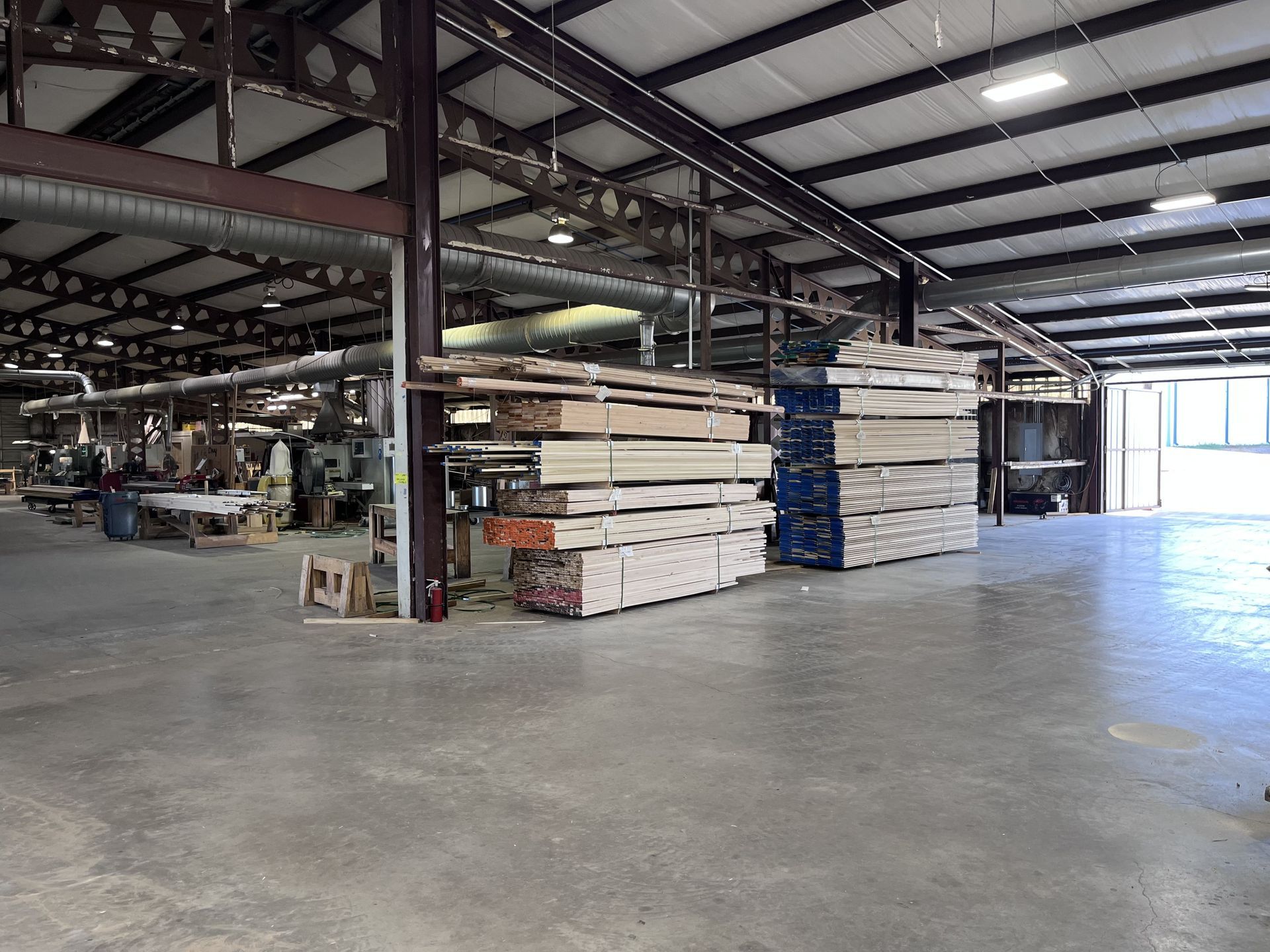 Warehouse interior with stacks of lumber, metal beams, and industrial equipment.