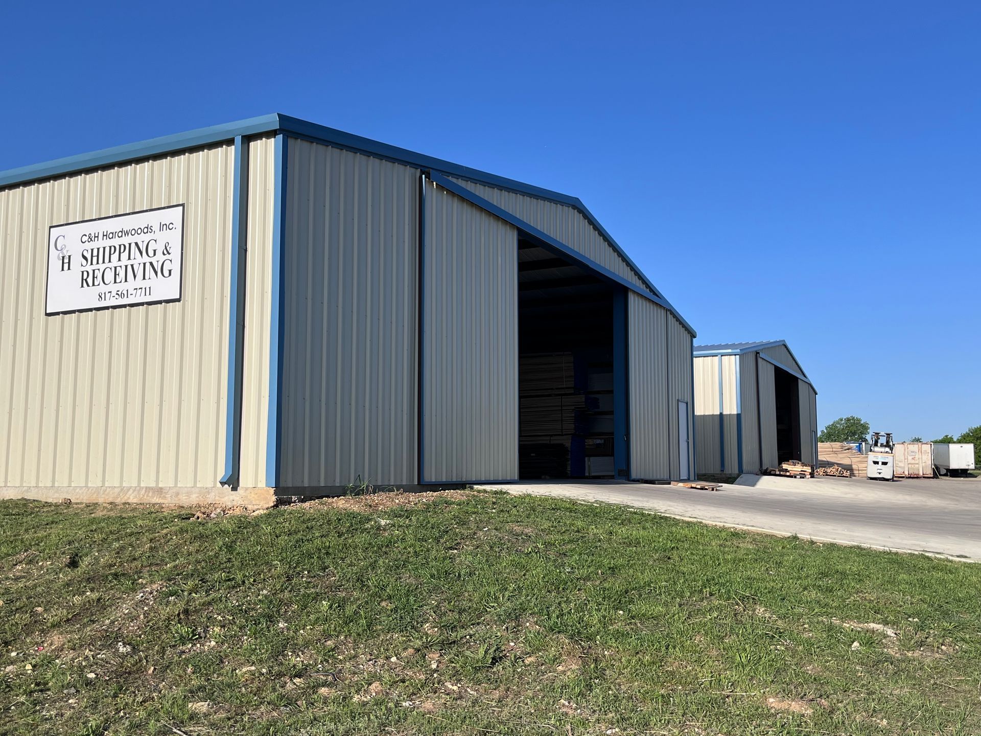 Metal warehouse buildings with blue trim under a clear, blue sky. A sign reads
