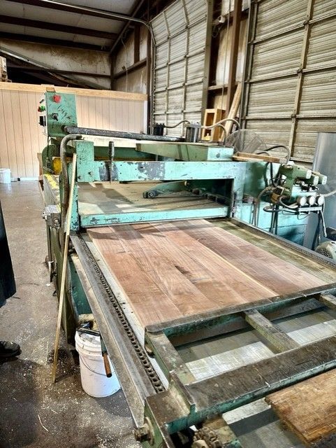 A large green industrial wood planer in a workshop, with wooden planks on the feed table.