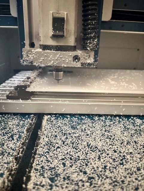A CNC machine cutting a white plastic sheet, producing white shavings.