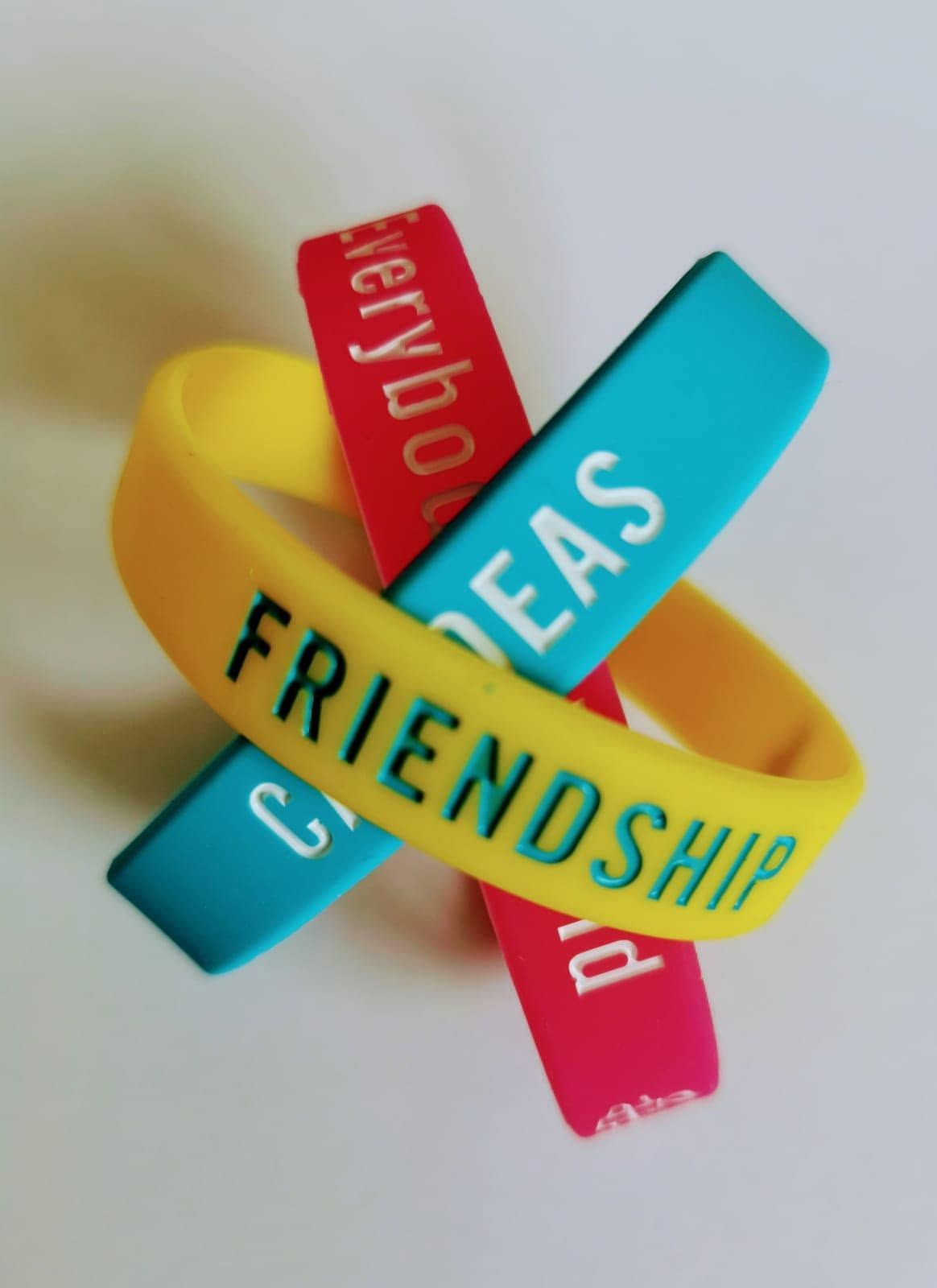 Yellow and turquoise bracelets with words “FRIENDSHIP” and “EAS” on a white background