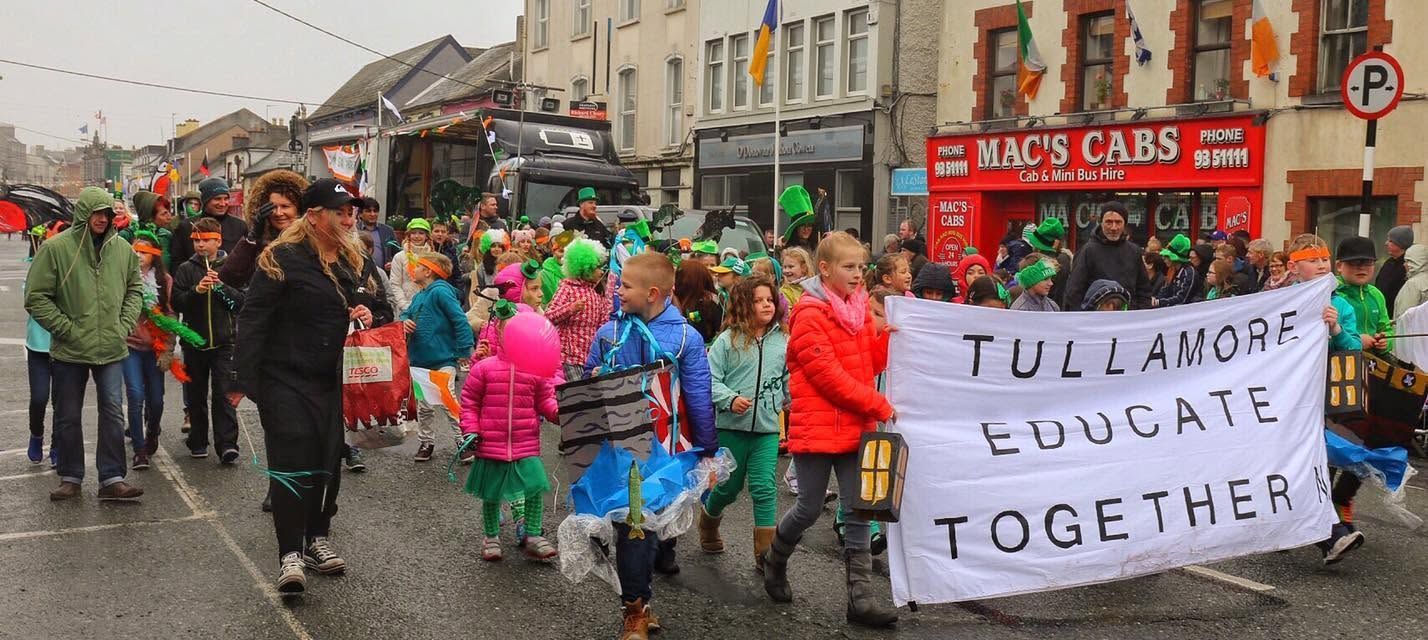 Crowd in rain holds “Education Together” banner during a street parade