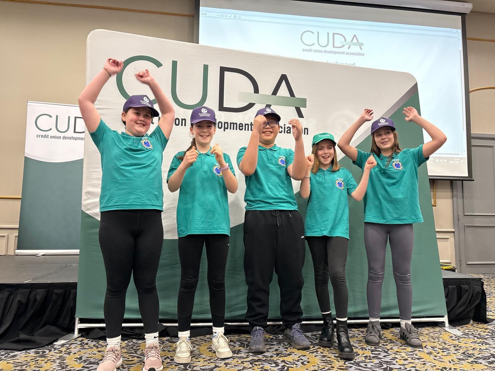 Five people in teal shirts pose with raised arms in front of a CUDA banner on a stage.