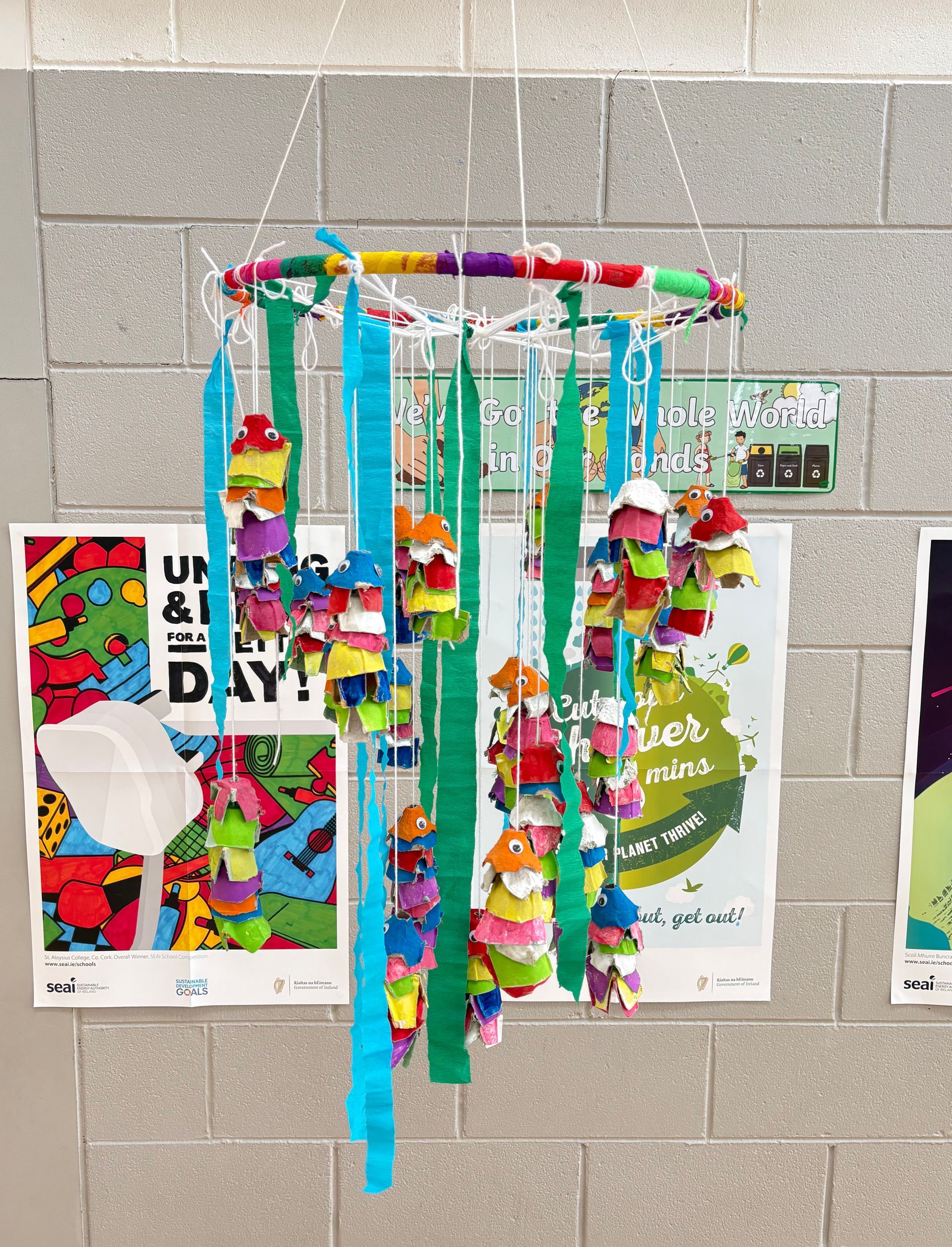 Colorful hanging paper craft with tassels and streamers displayed on a wall of posters.