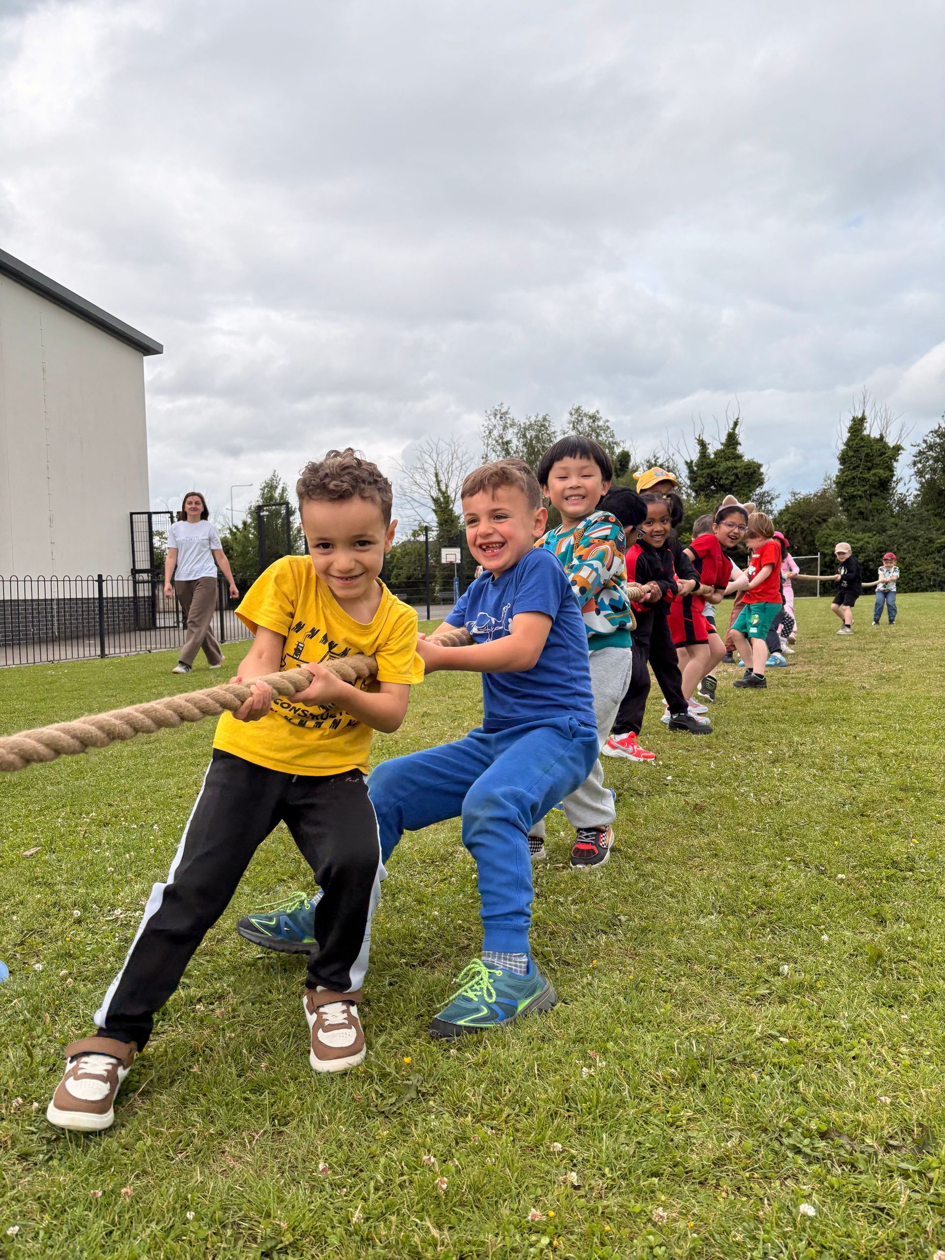 Children playing tug-of-war on a grassy field outdoors, smiling and leaning back together.