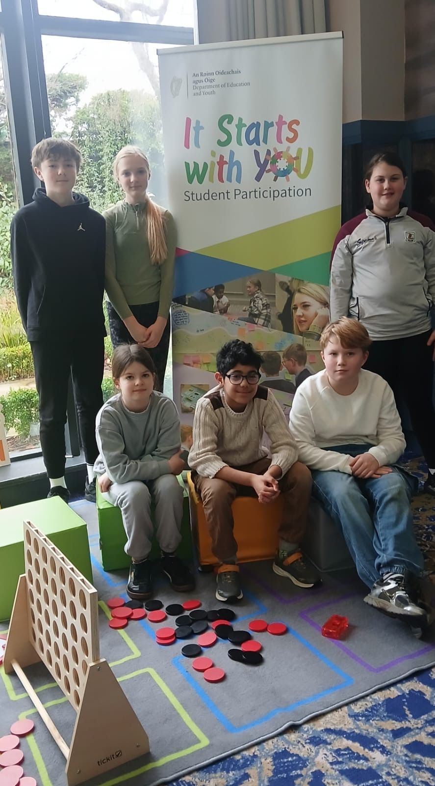 Group posing beside sign reading “It Starts with” at a colorful floor activity area
