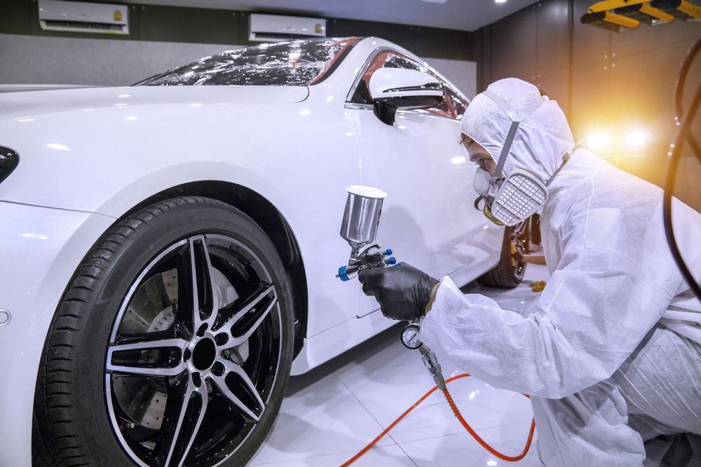 Person in Protective Suit Spraying White Paint on a White Car — Mid Coast Smash Repairs In Forster, NSW