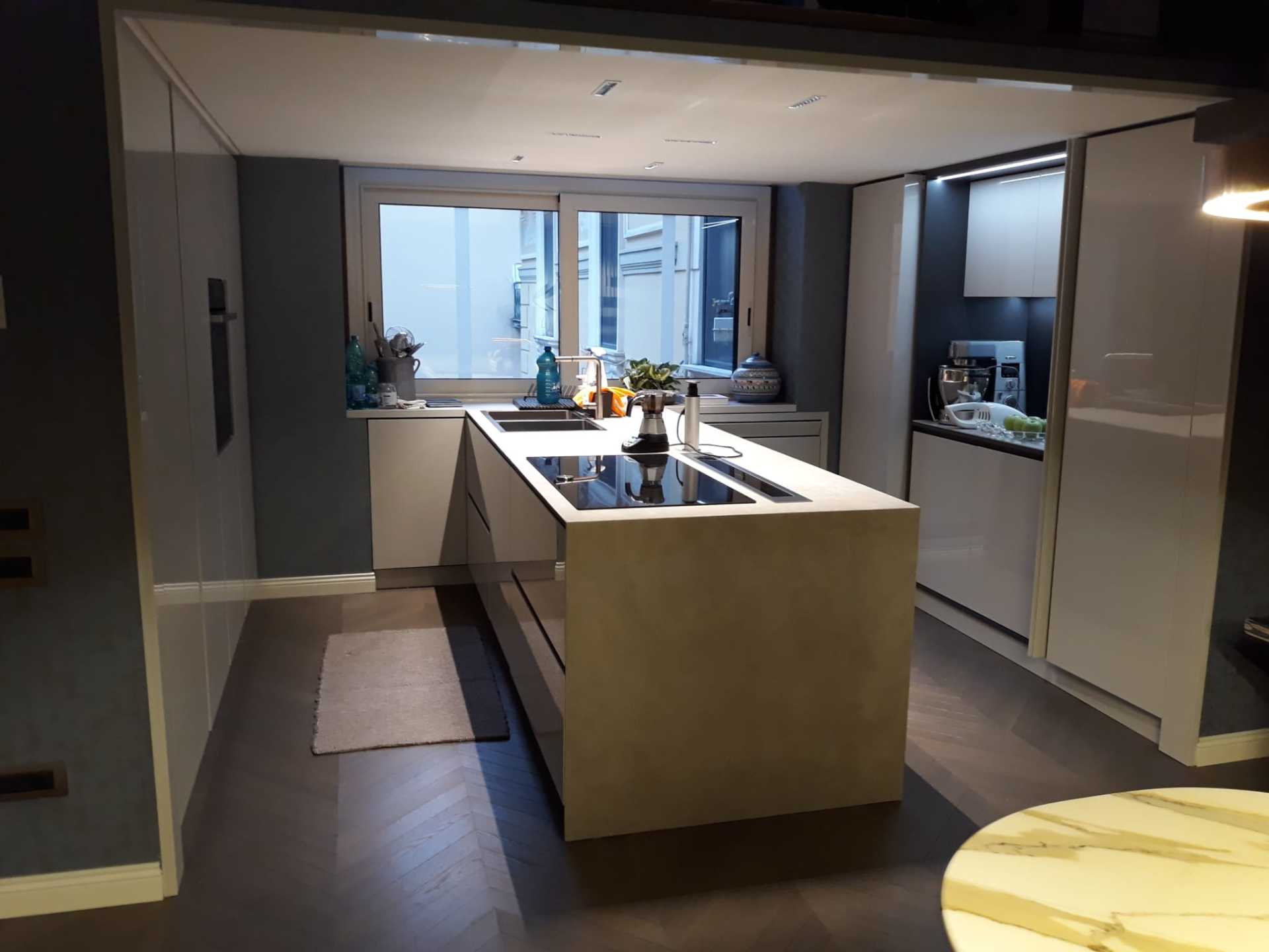 Cucina moderna con isola, mobili bianchi, pavimento in legno scuro e finestra.