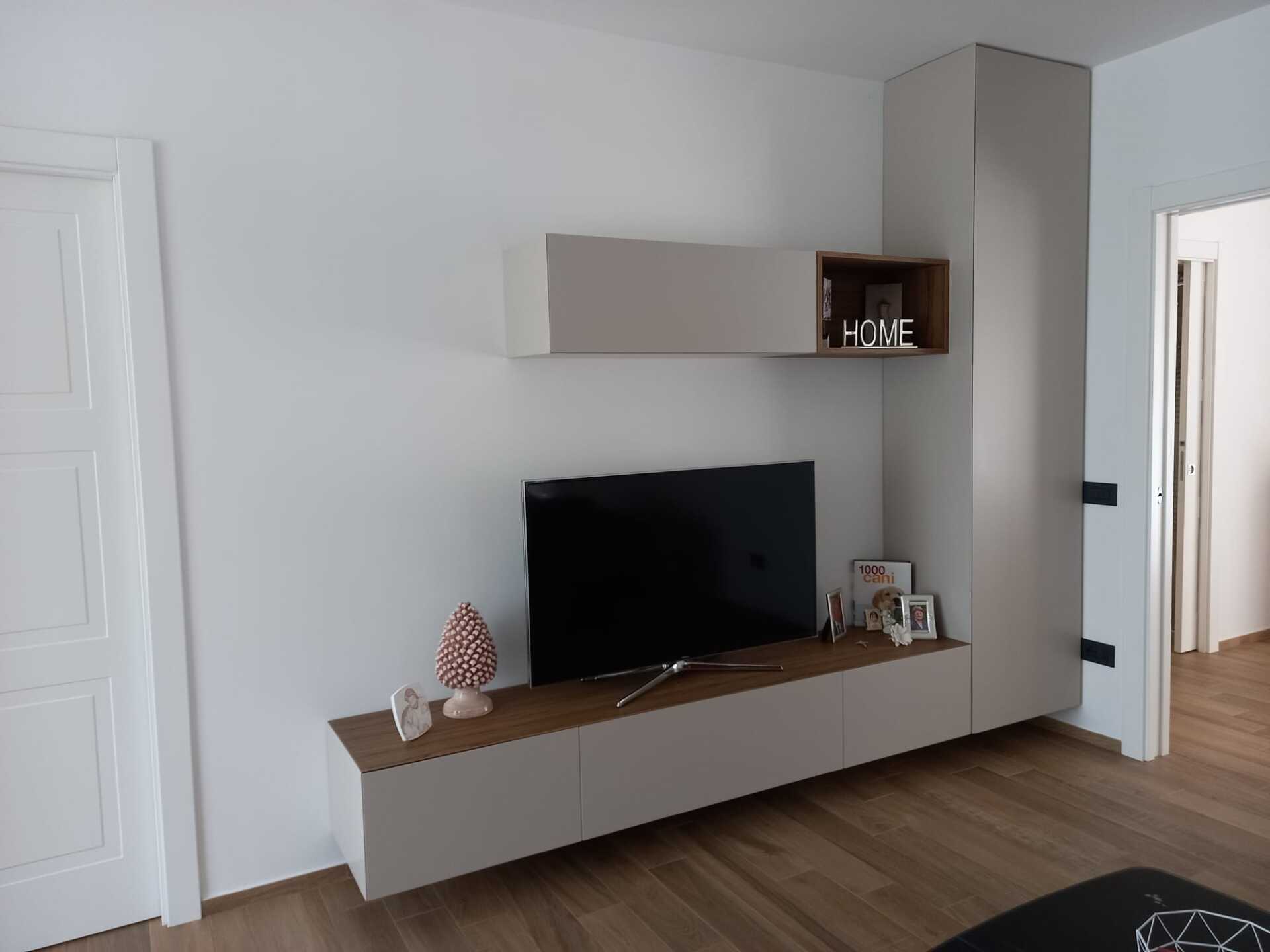 Soggiorno con TV montata, mensole sospese e pavimento in legno.