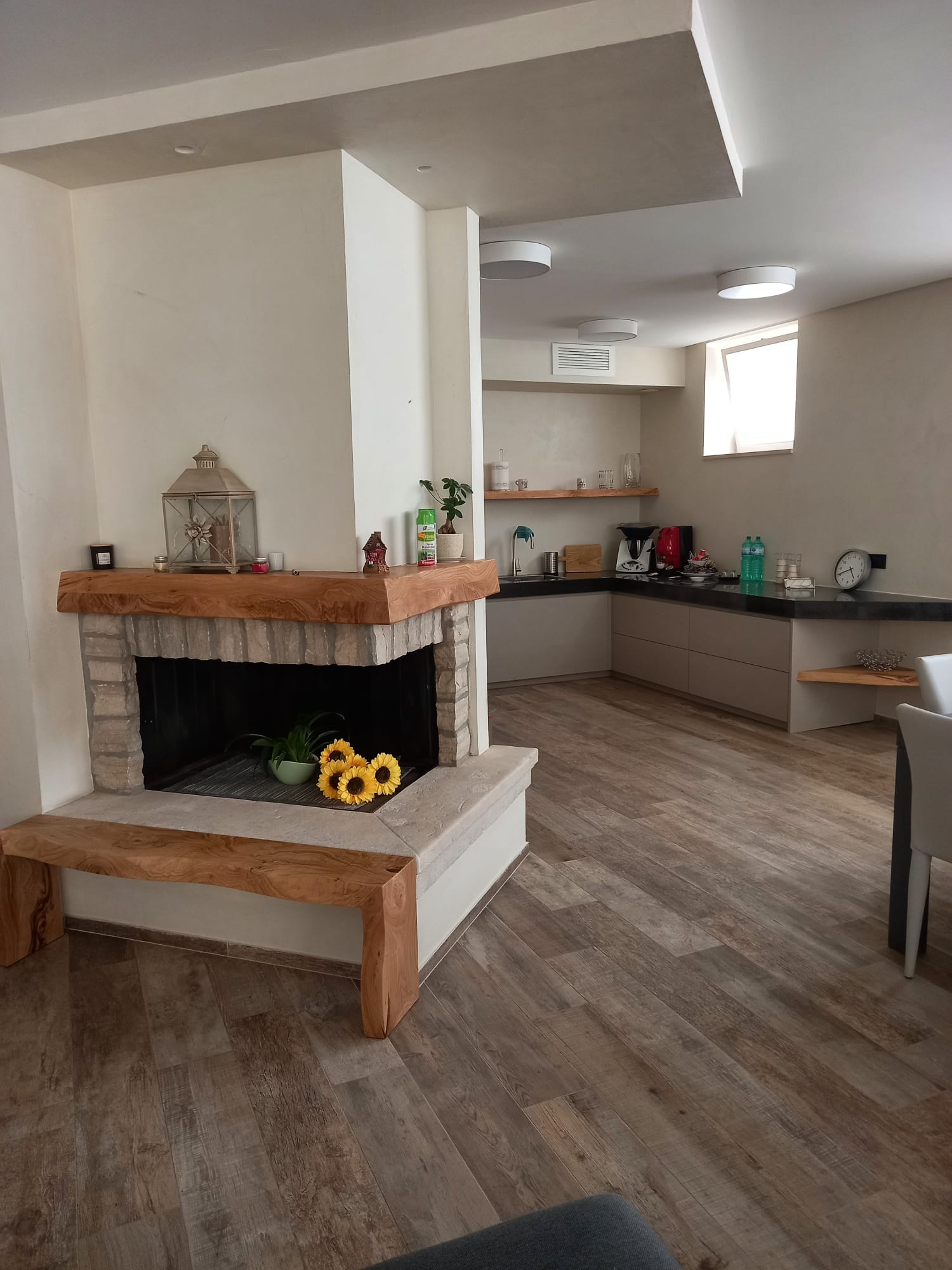 Interni accoglienti: camino con panca in legno, che conduce alla cucina con ripiani, pavimenti in legno chiaro.