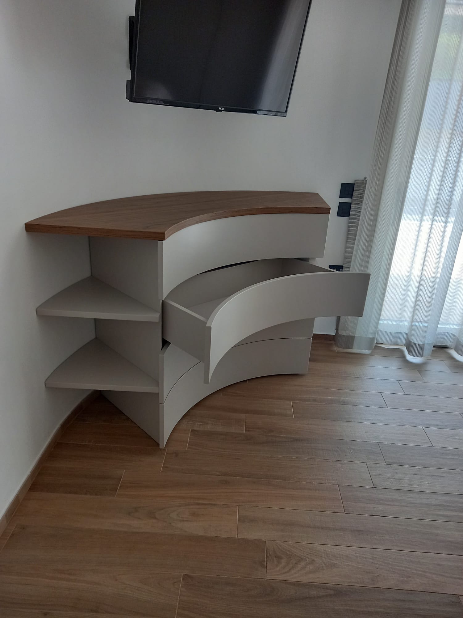Mobile angolare con ripiani curvi e cassetto, piano in legno, vernice grigia, TV sopra, pavimento in legno.