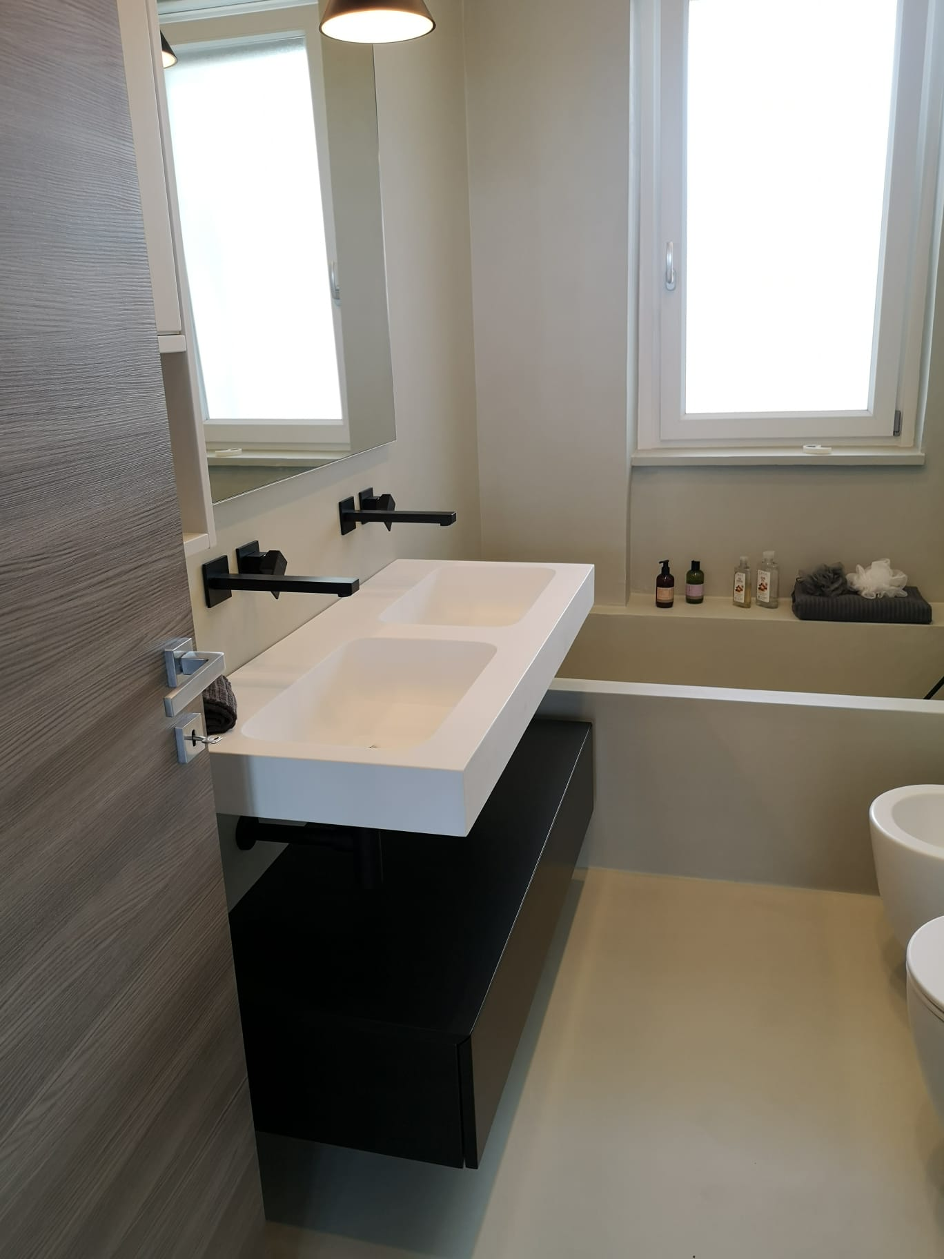 Bagno moderno con lavandino bianco, rubinetto nero e mobiletto; sullo sfondo c'è una vasca da bagno.