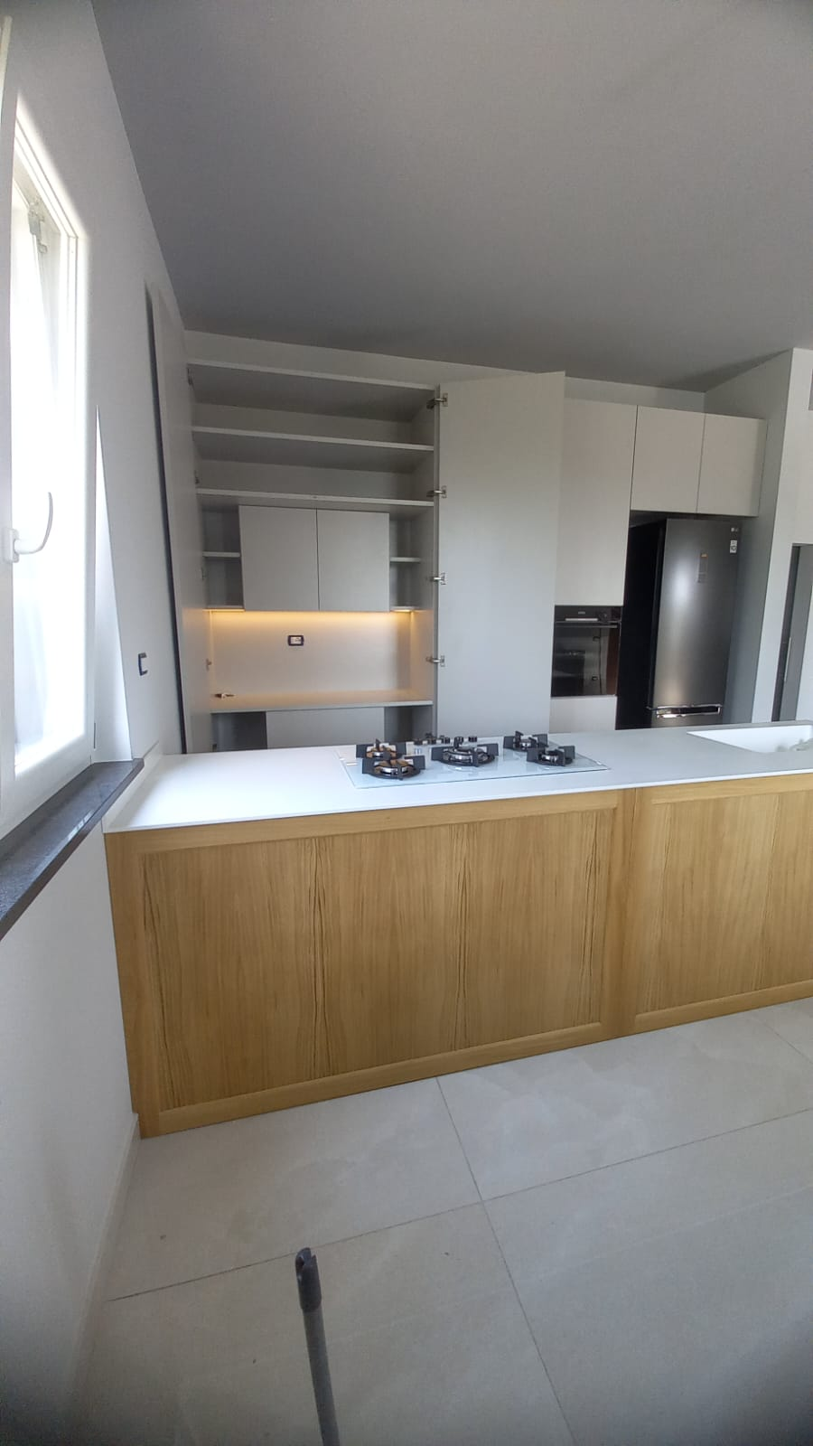 Cucina moderna con isola in legno chiaro, ripiani bianchi ed elettrodomestici in acciaio inossidabile.