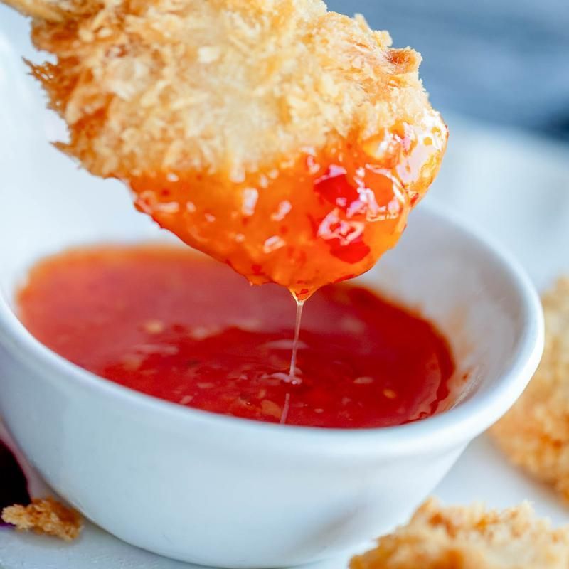 Crispy fried snack being dipped into a white bowl of red sauce