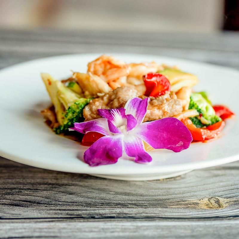 Plated gourmet dish with shrimp, vegetables, and a purple orchid garnish on a white plate