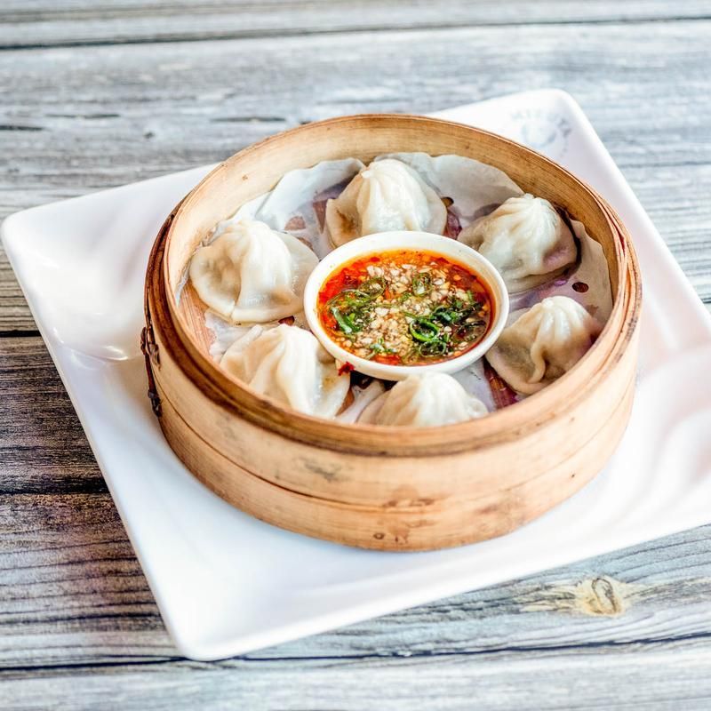Steamed dumplings in a bamboo basket with dipping sauce on a white plate