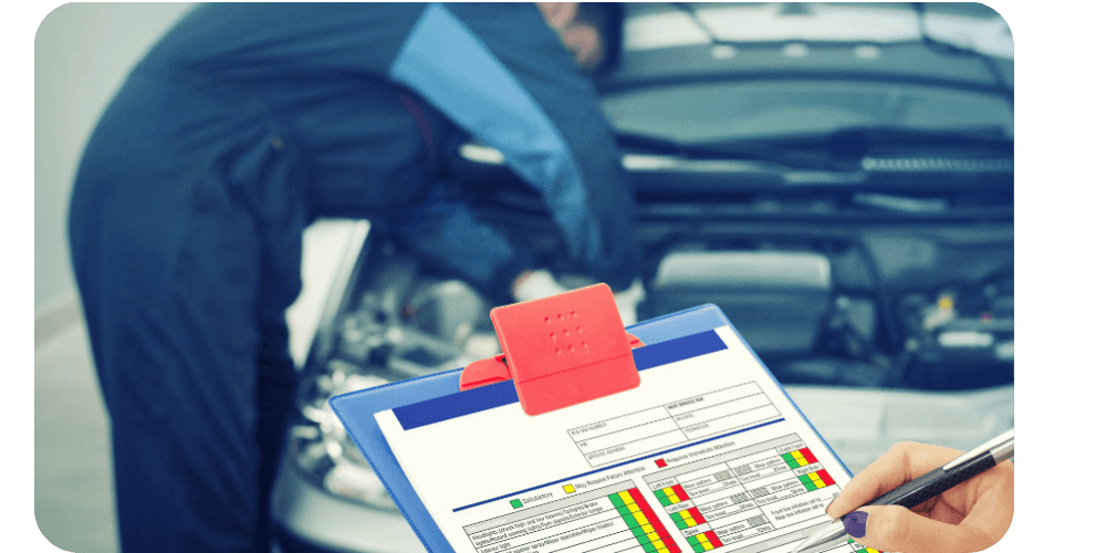 Mechanic in blue jumpsuit works on car engine while someone reviews a checklist on a clipboard.