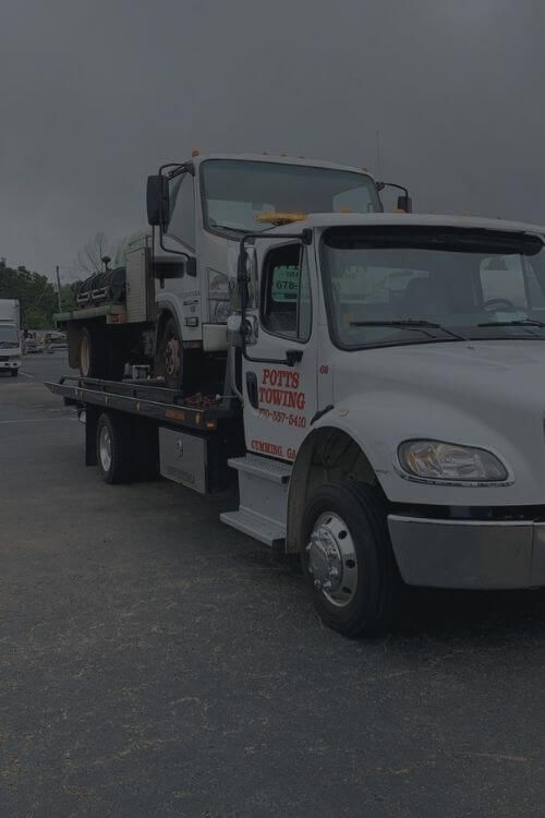 Tow truck carrying another truck; overcast sky; parking lot.