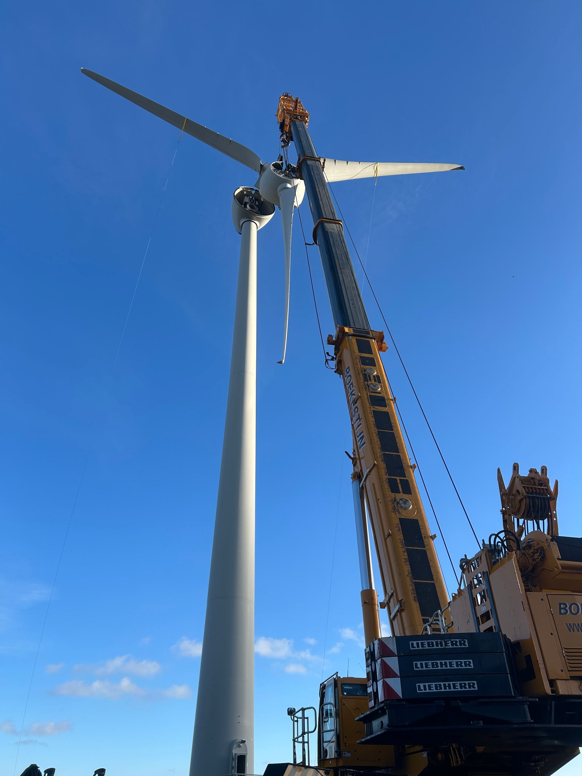 Wind turbine being installed by a crane against a clear blue sky.