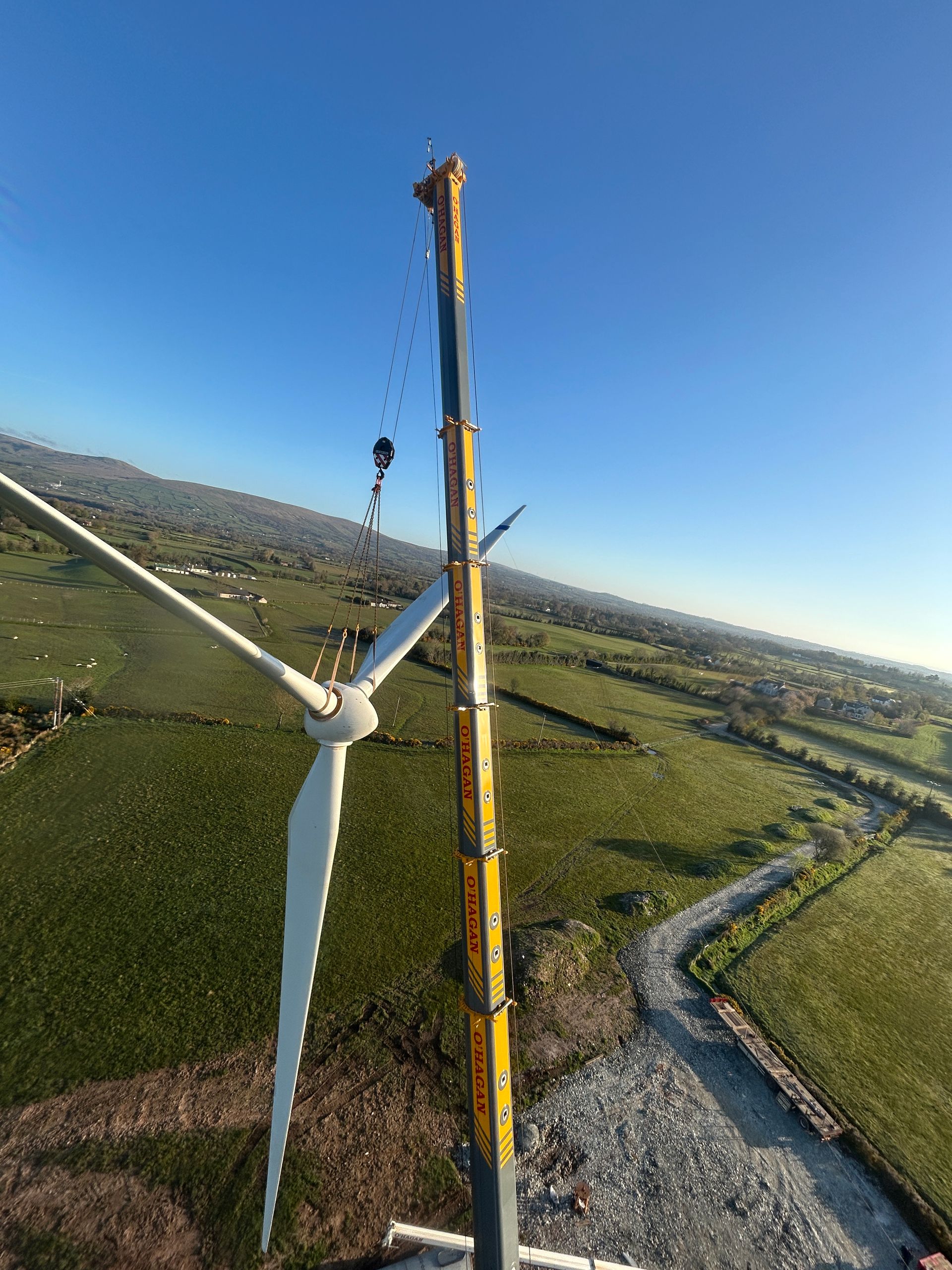 Wind turbine being inspected beside a yellow tower in a green rural landscape under a clear blue sky
