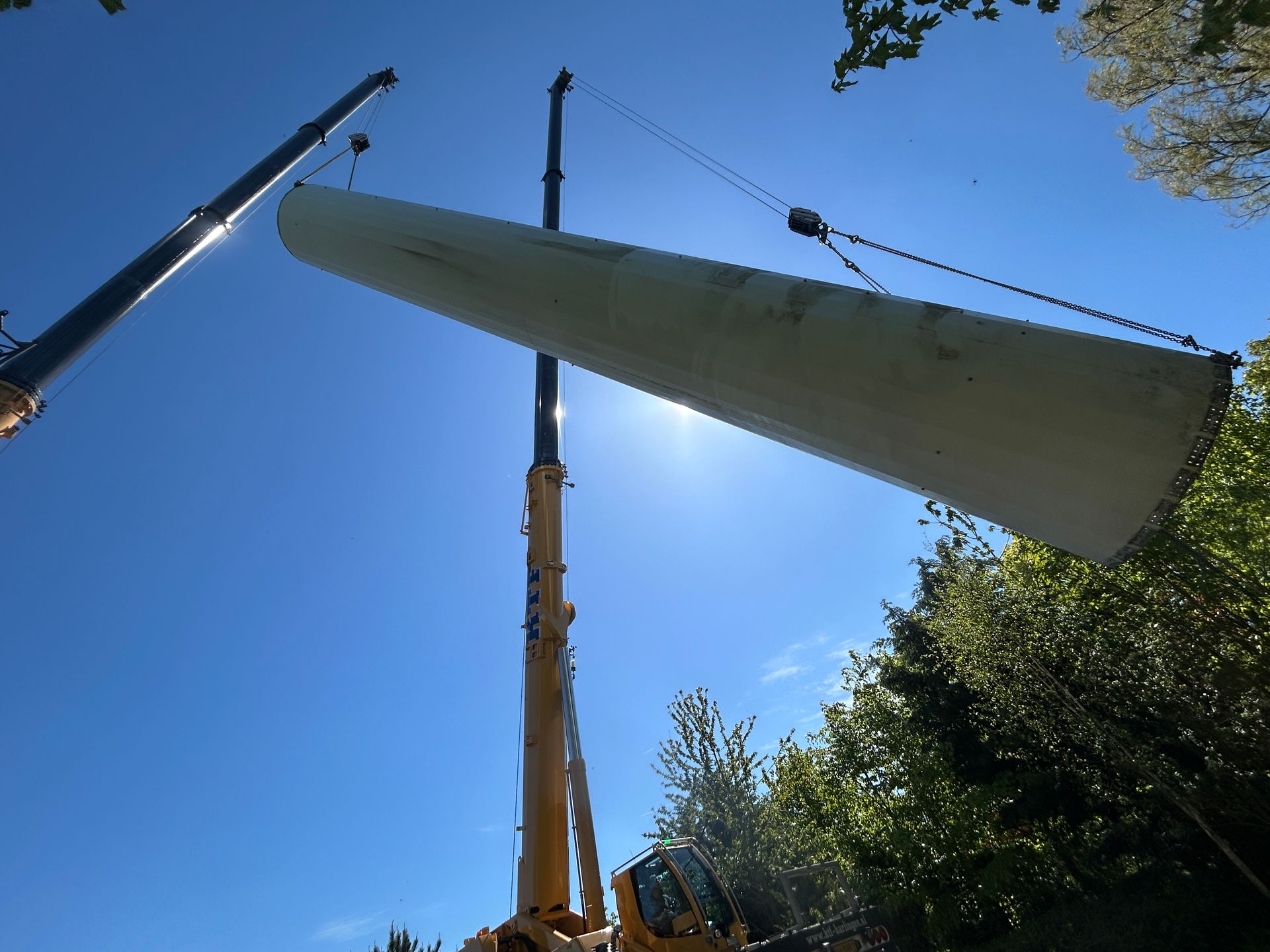 Large white sail being hoisted by a crane against a bright blue sky, viewed from below