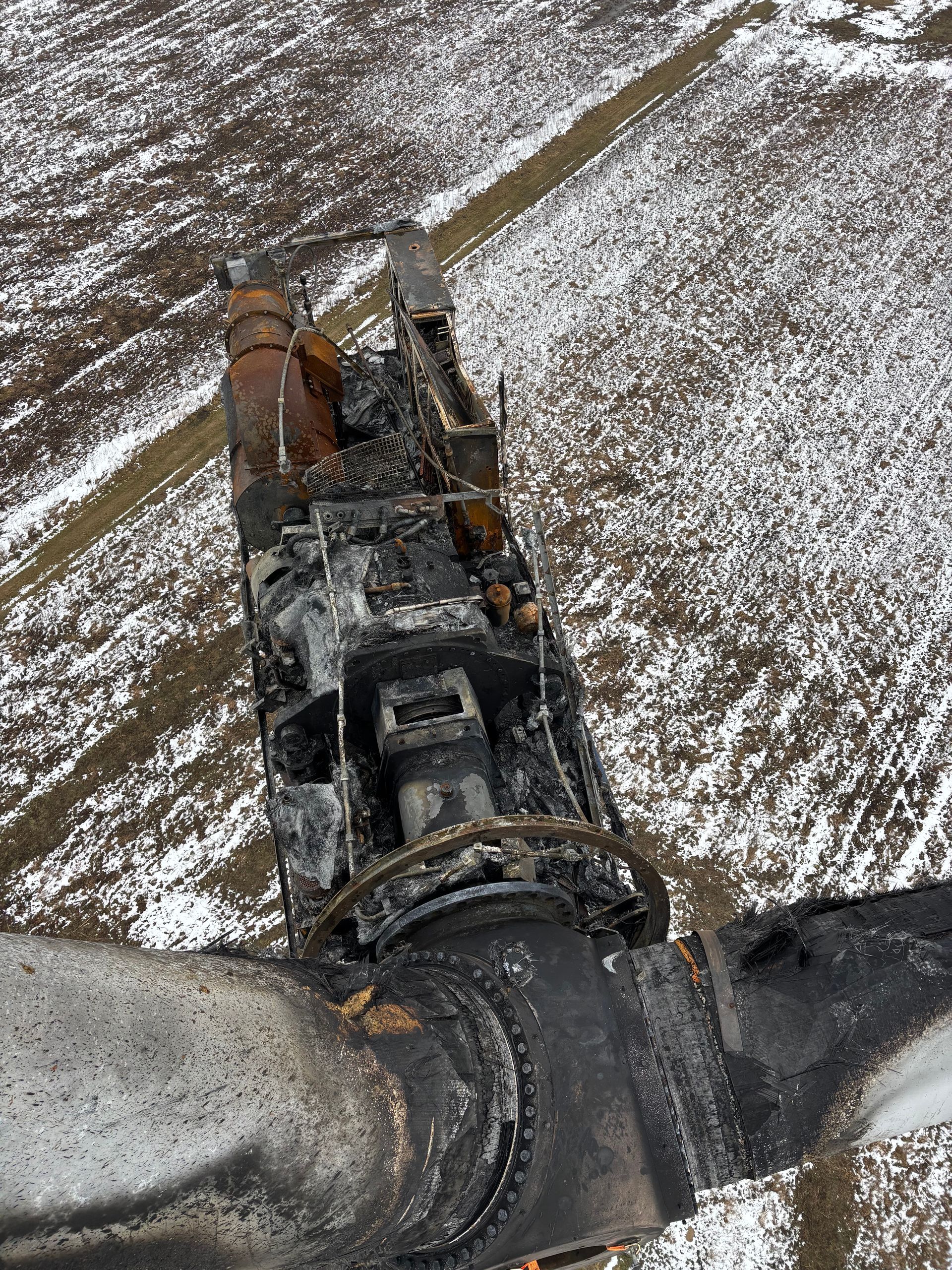 Aerial view of a damaged train car on snowy tracks with debris and rusted machinery.