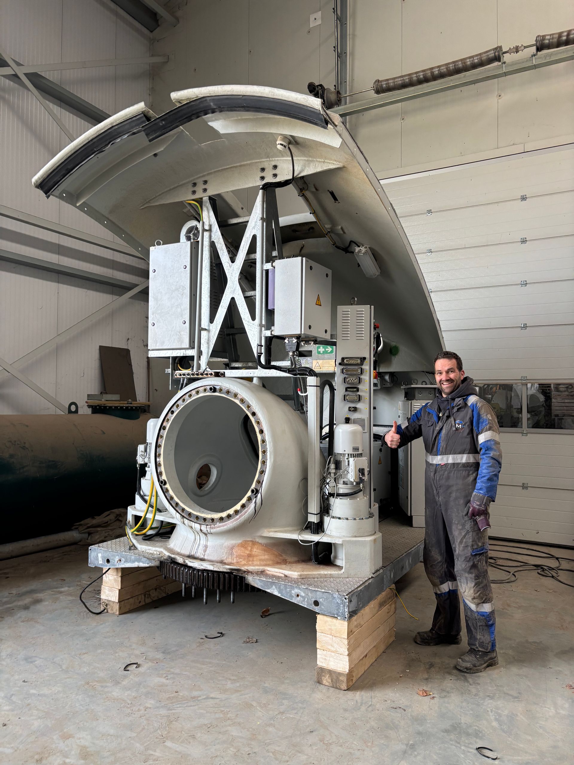 Person stands beside a large industrial machine in a warehouse-like workshop.