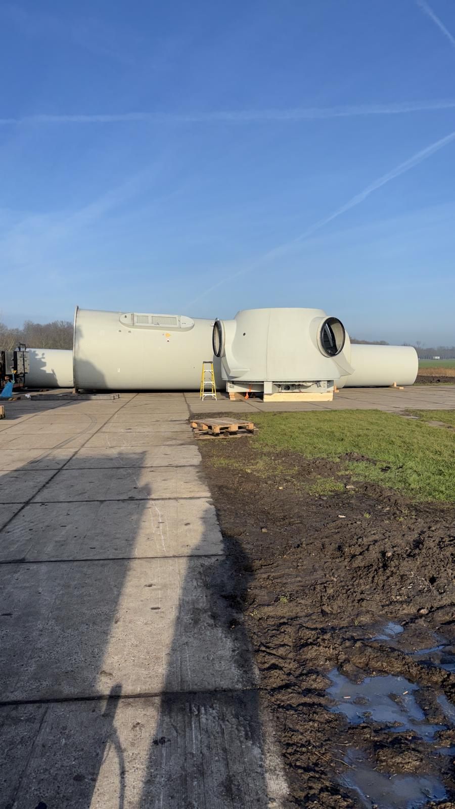 Two large white industrial trailers on a gravel lot under a blue sky, with a muddy puddle in the foreground