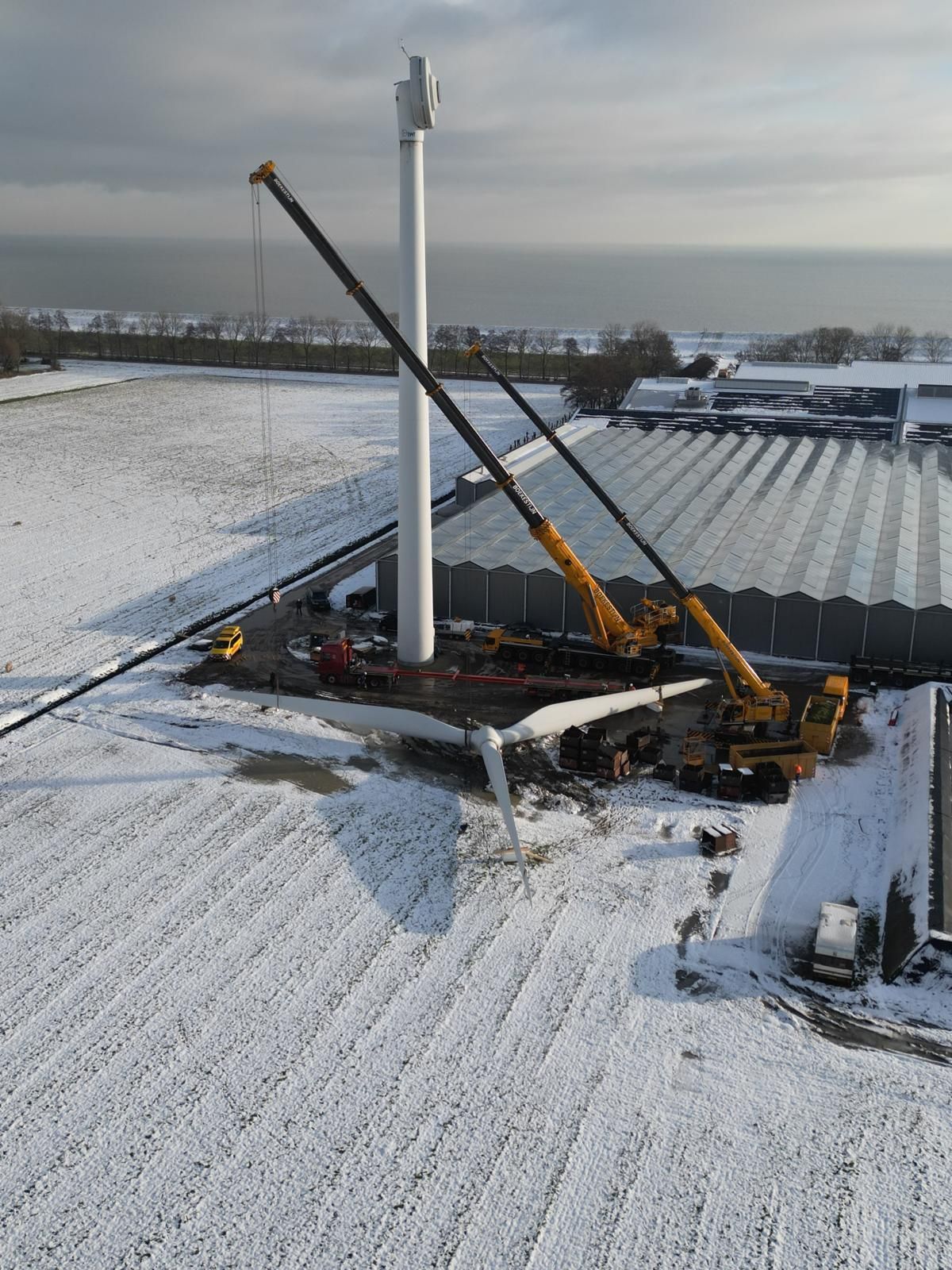 Construction crane on a snowy industrial rooftop beside a tall white tower.