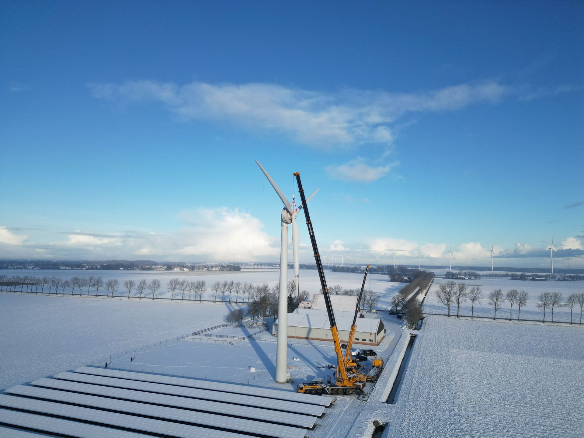 Snow-covered field with two wind turbines under a blue sky and clouds