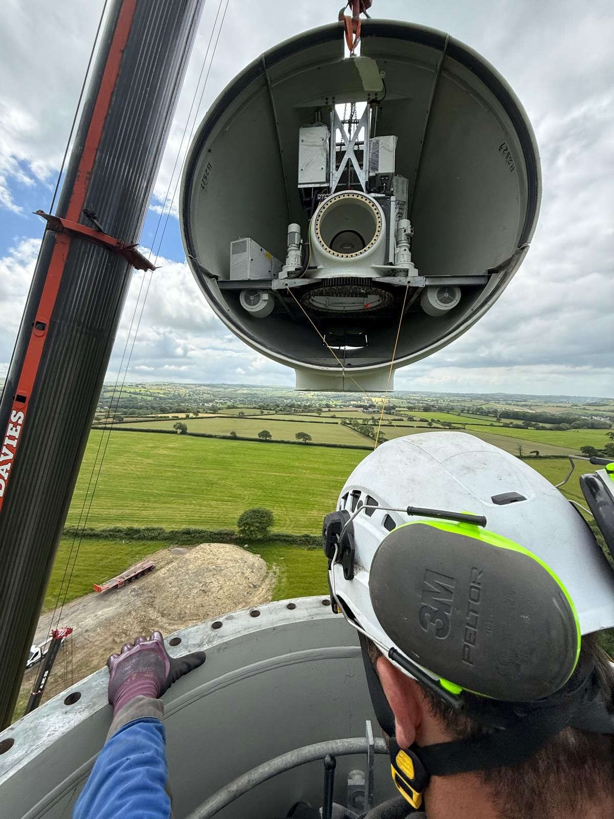 Worker looking into a large wind turbine nacelle from the top of a wind tower over a green landscape