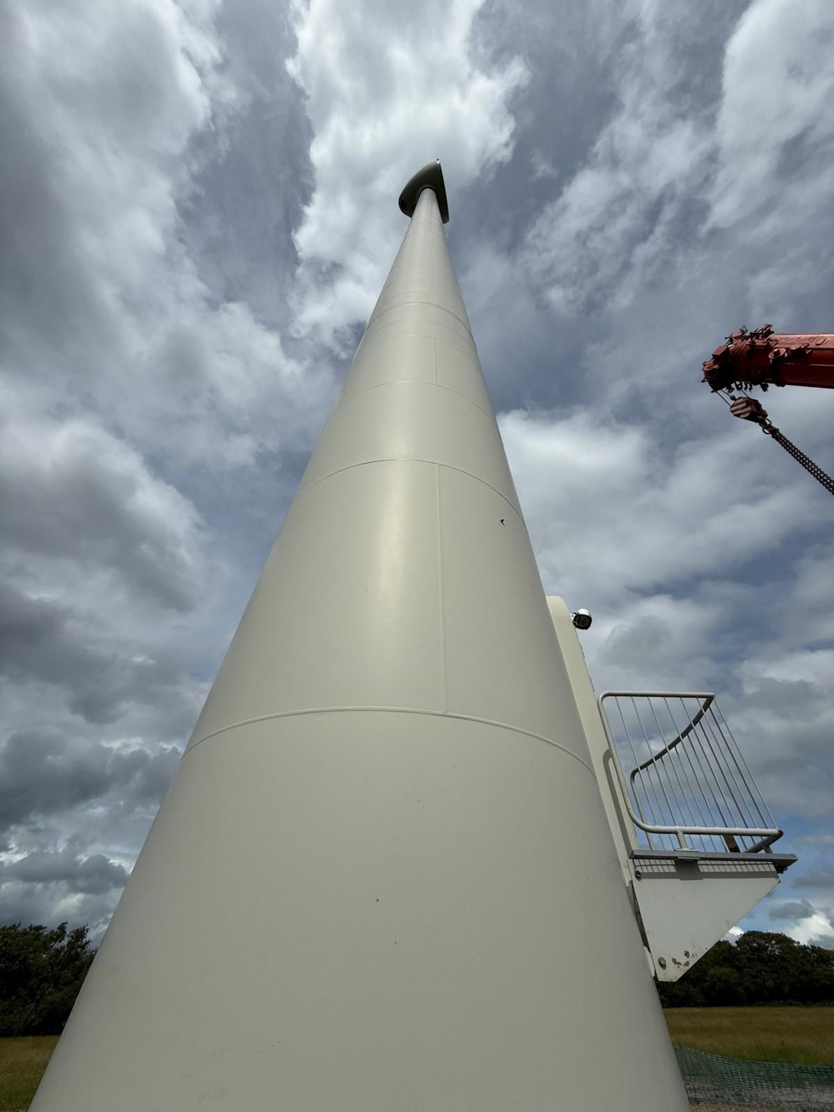 Tall white wind turbine tower shot from below against a cloudy sky