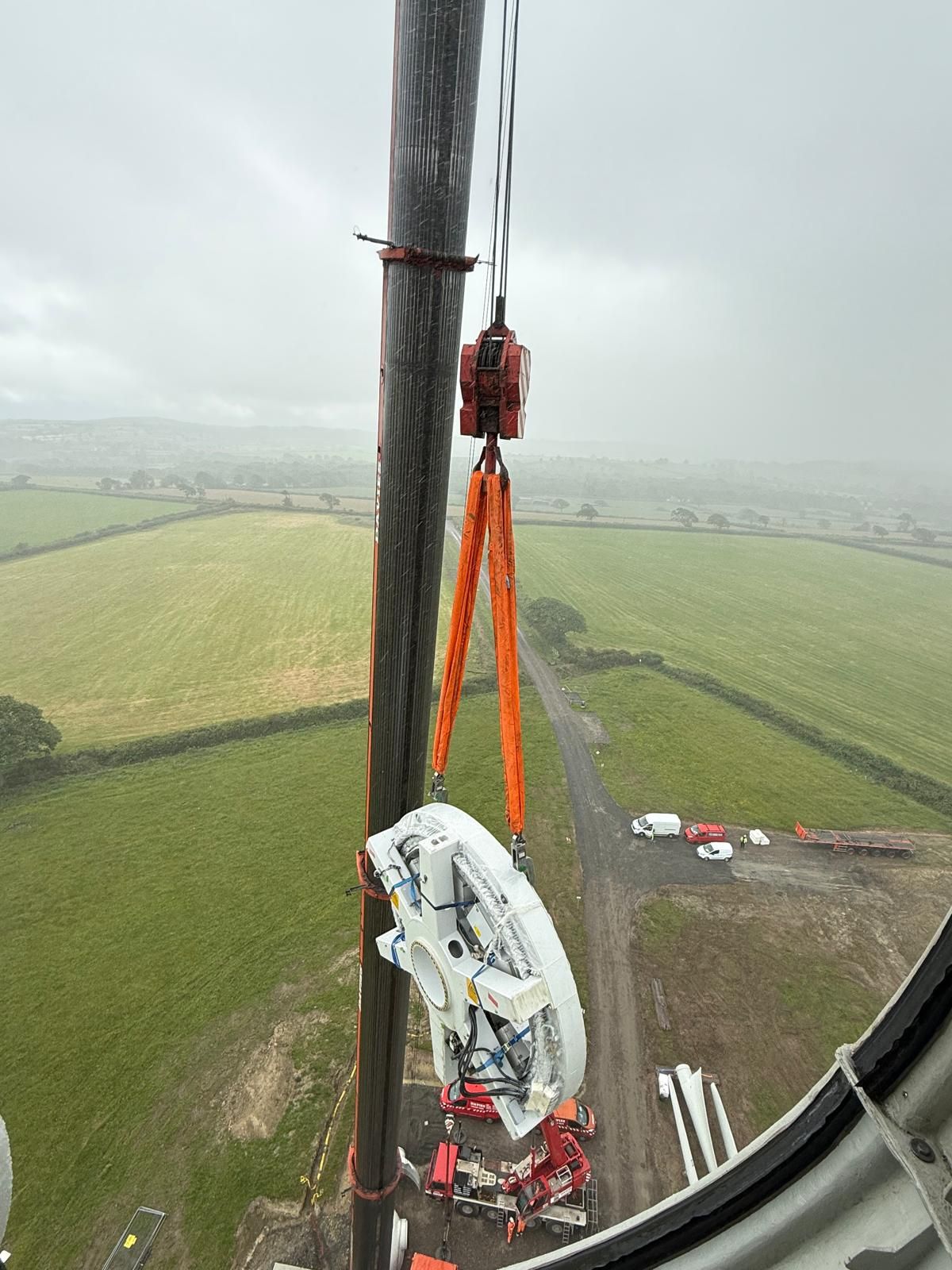 Aerial view from a wind turbine showing two workers on a tower above green fields and a cloudy landscape