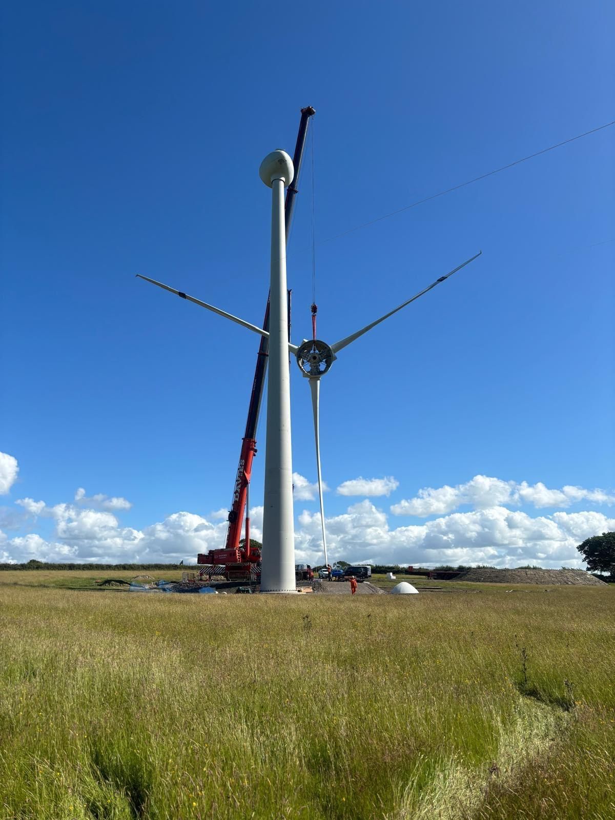 Wind turbine being installed in a grassy field, with a crane under a bright blue sky.