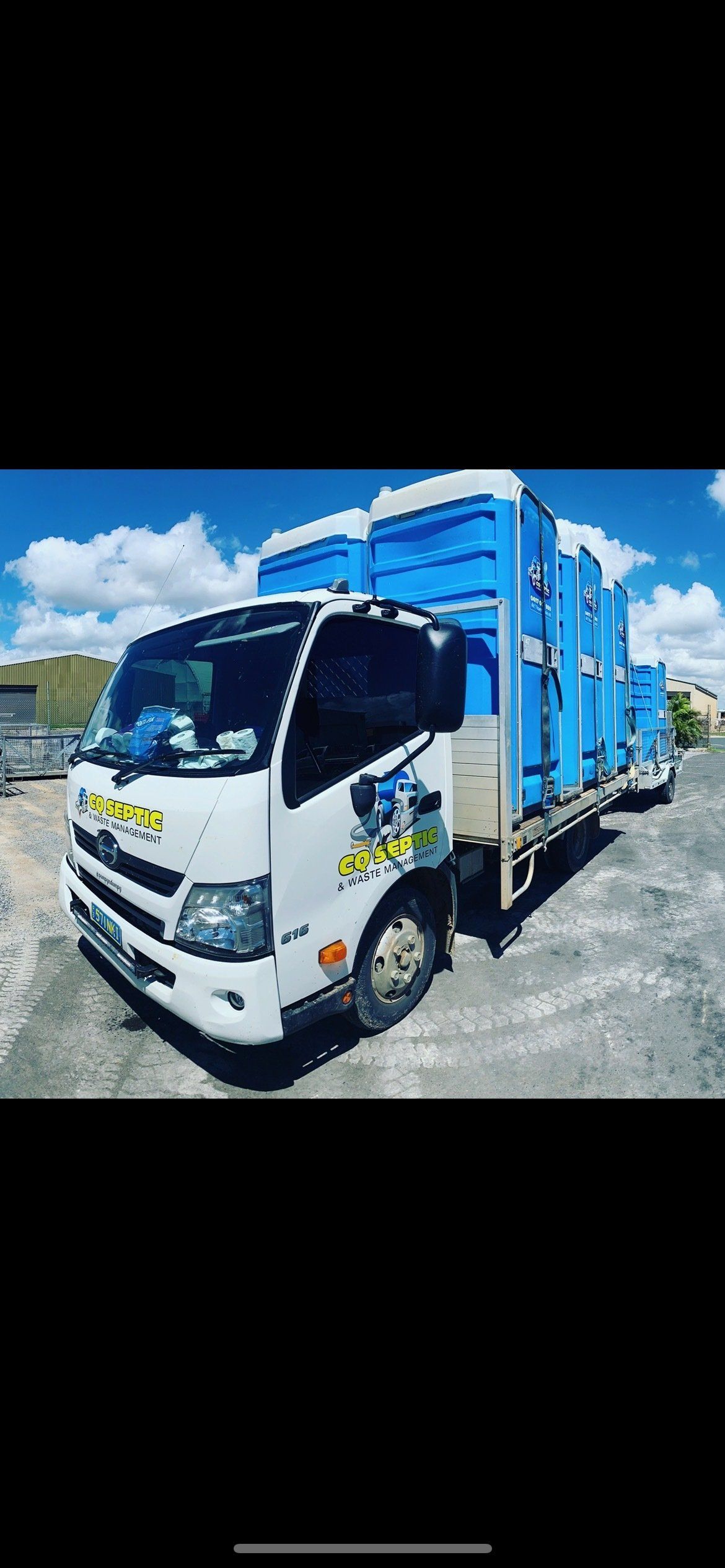 A white truck is parked next to a row of blue portable toilets.